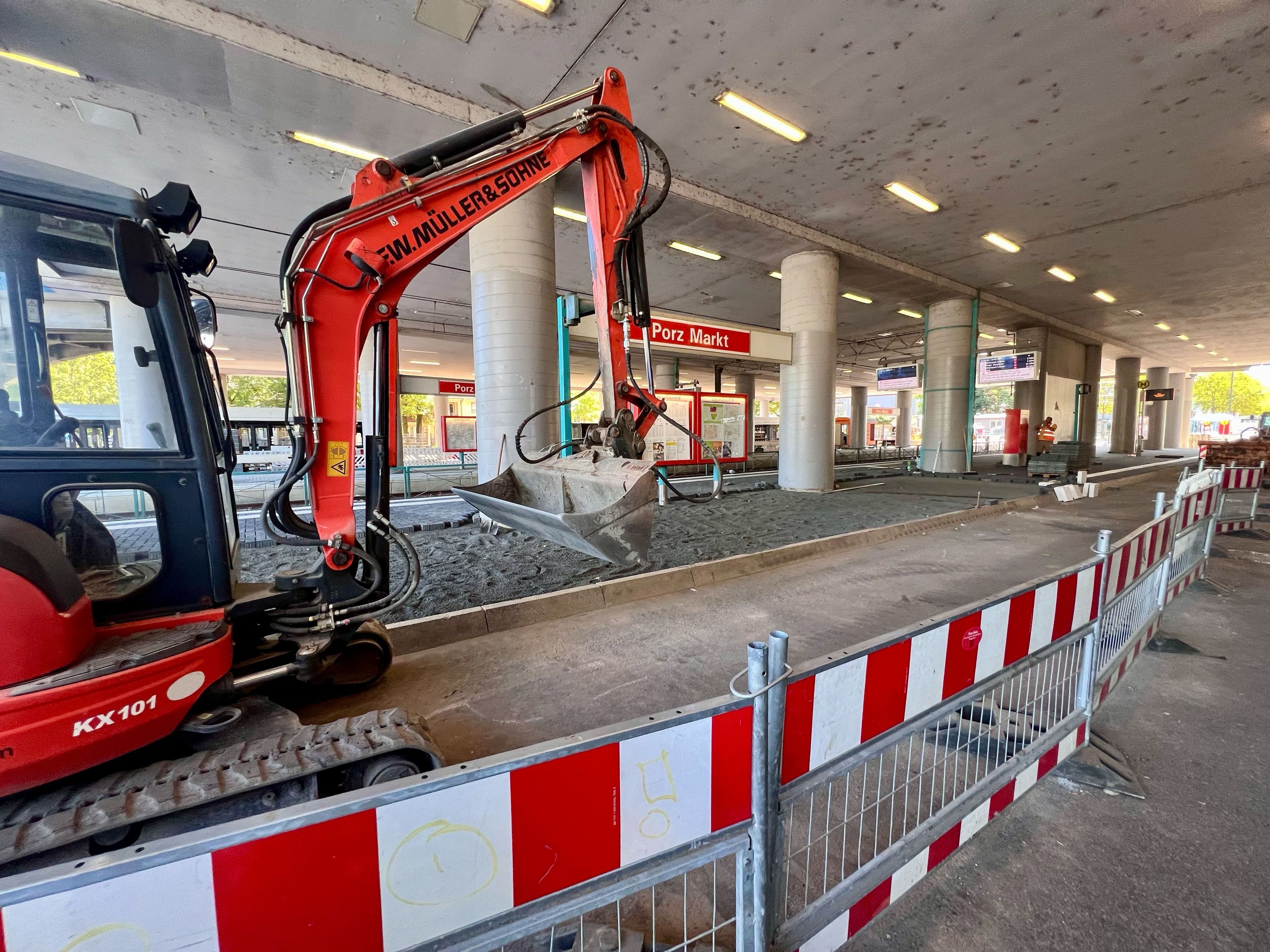 Ein Bagger steht an der Haltestelle Porz Markt, drumherum rot-weiße Absperrgitter.