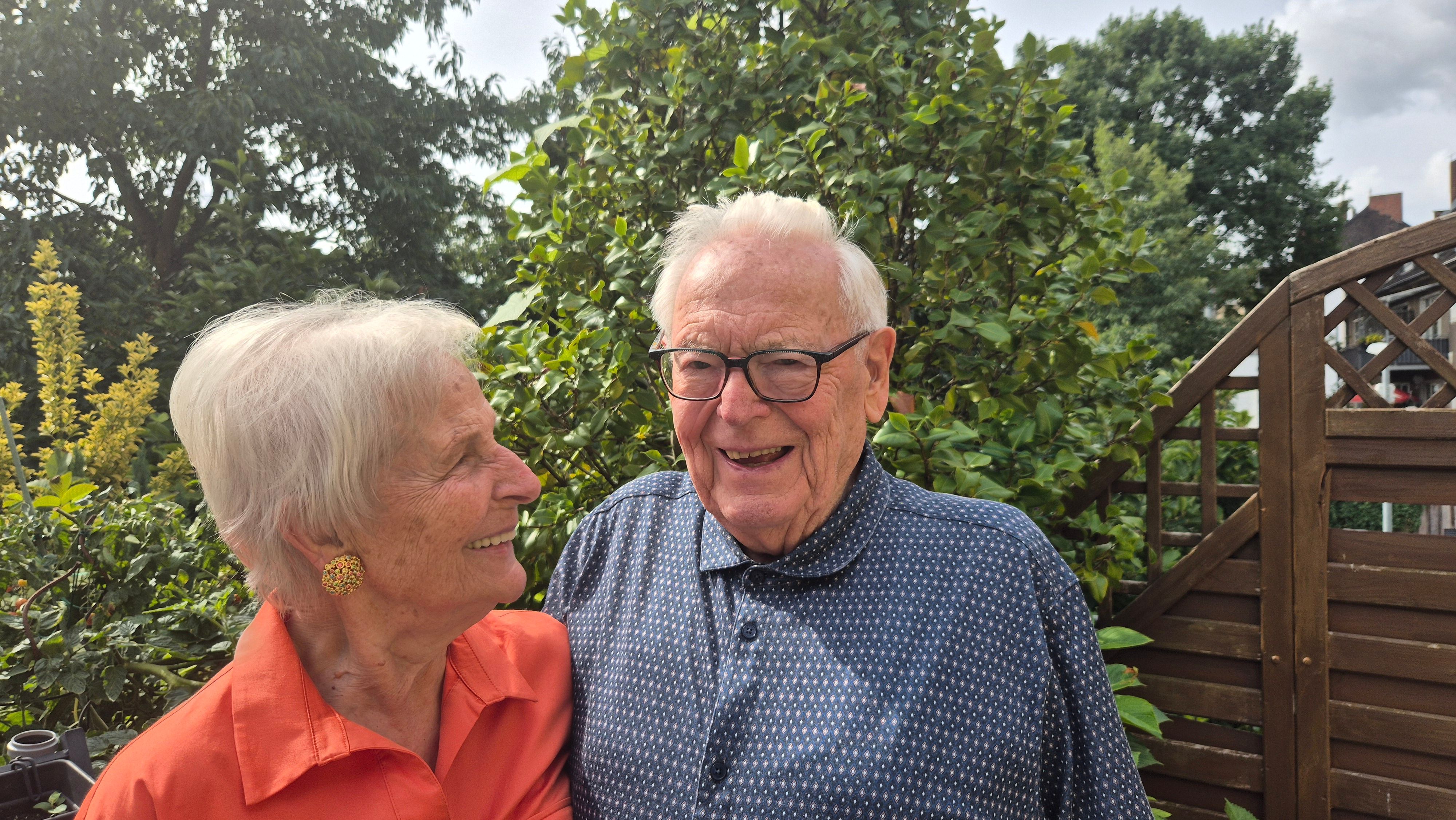 Eine ältere Frau und ein älterer Mann stehen lachend nebeneinander.