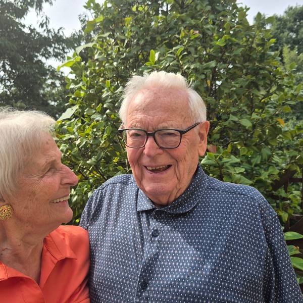 Eine ältere Frau und ein älterer Mann stehen lachend nebeneinander.
