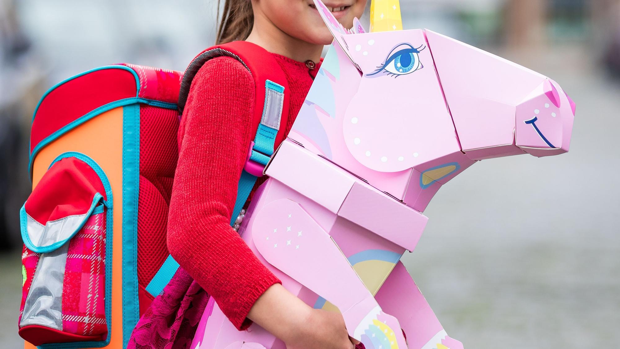 Eine Erstklässlerin steht mit Ranzen und Einhorn-Schultüte am Tag ihrer Einschulung vor der Schule.