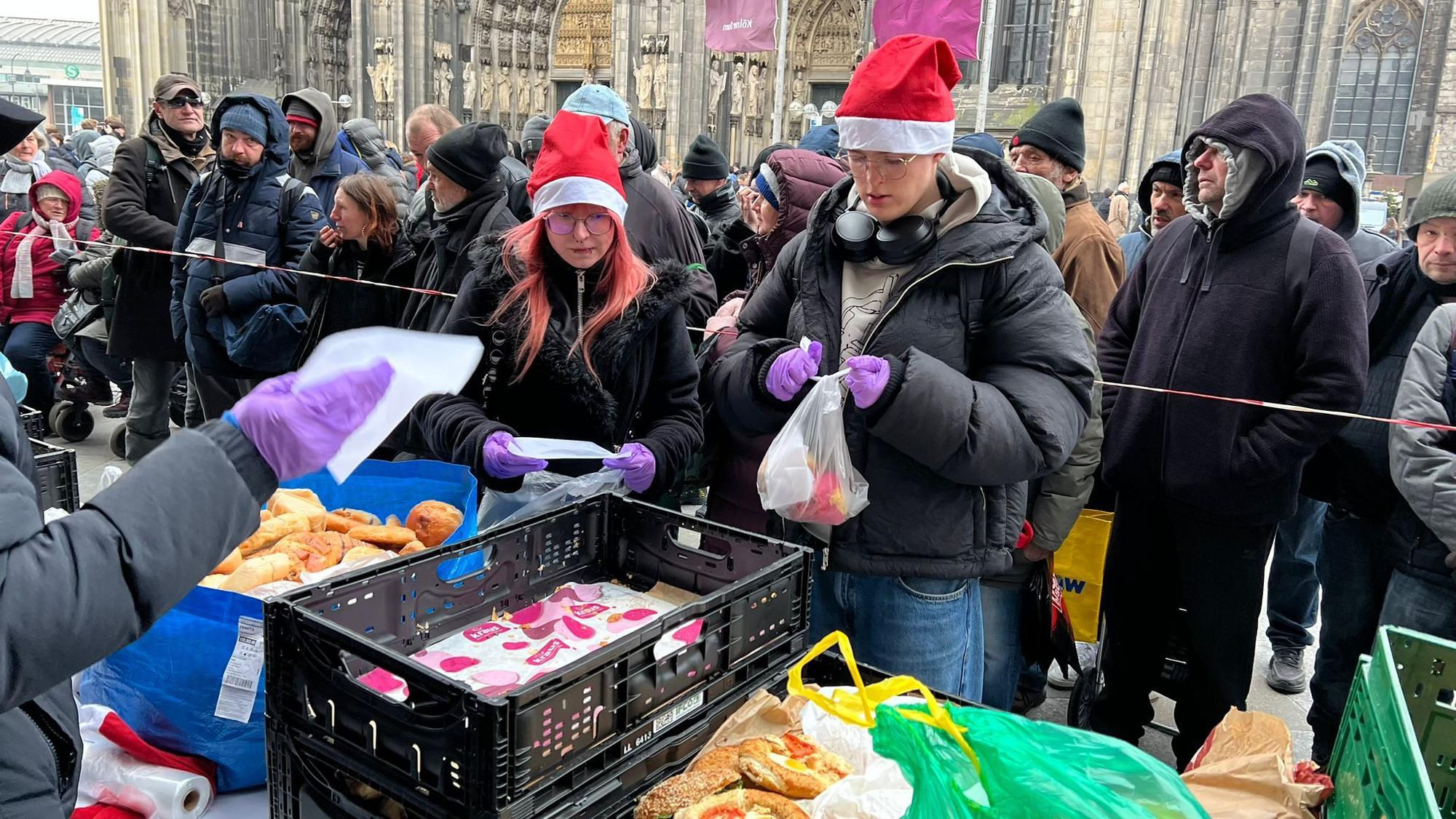 Im Jahr 2024 verteilen Schüler des Berufskolleg an der Lindenstraße mit Juttas Suppenküche Essen an Bedürftige. Sie stehen auf der Domplatte und tragen Weihnachtsmützen.