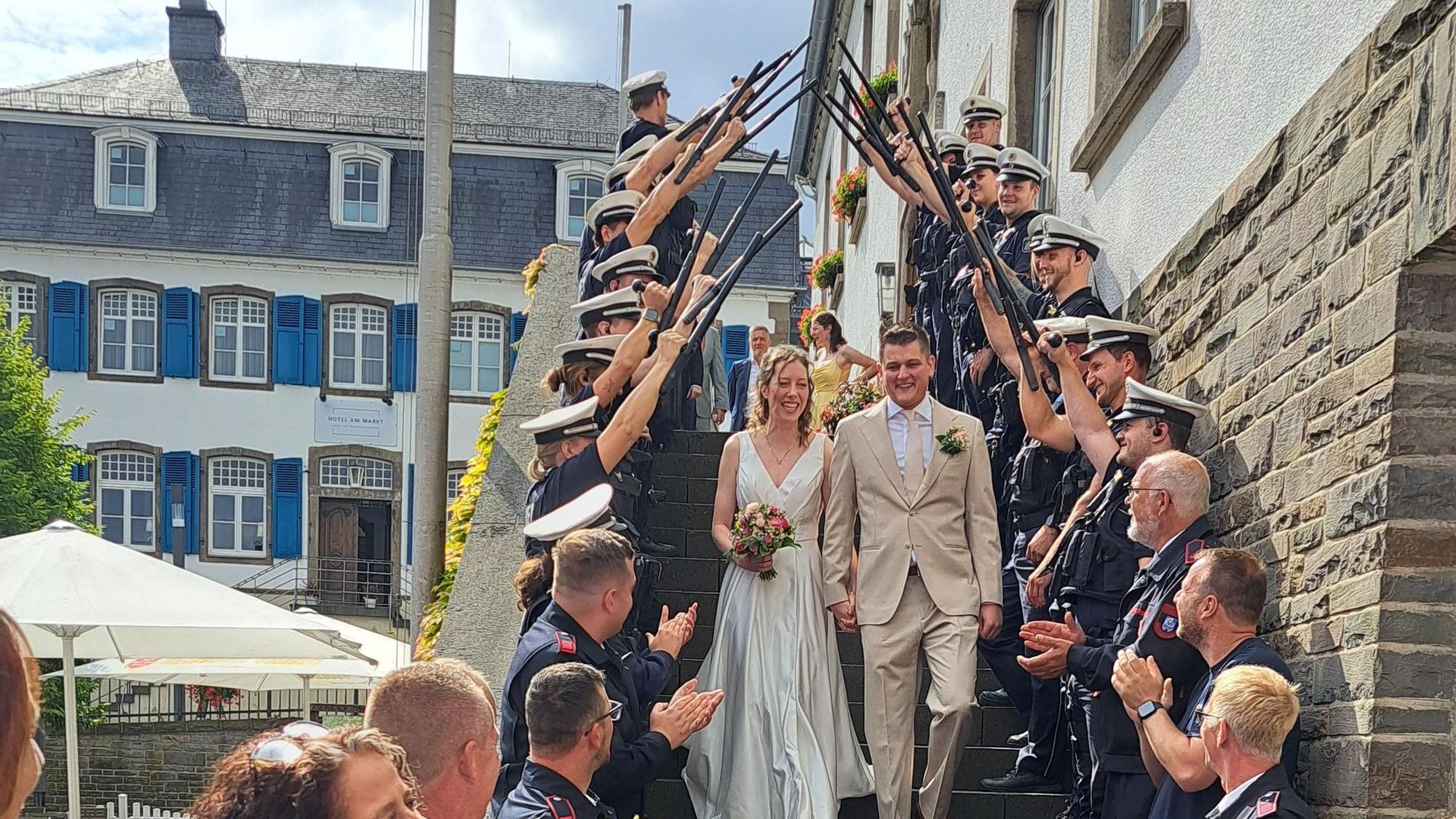 Das Foto zeigt ein Brautpaar, Polizisten und feuerwehrleute stehen Spalier.