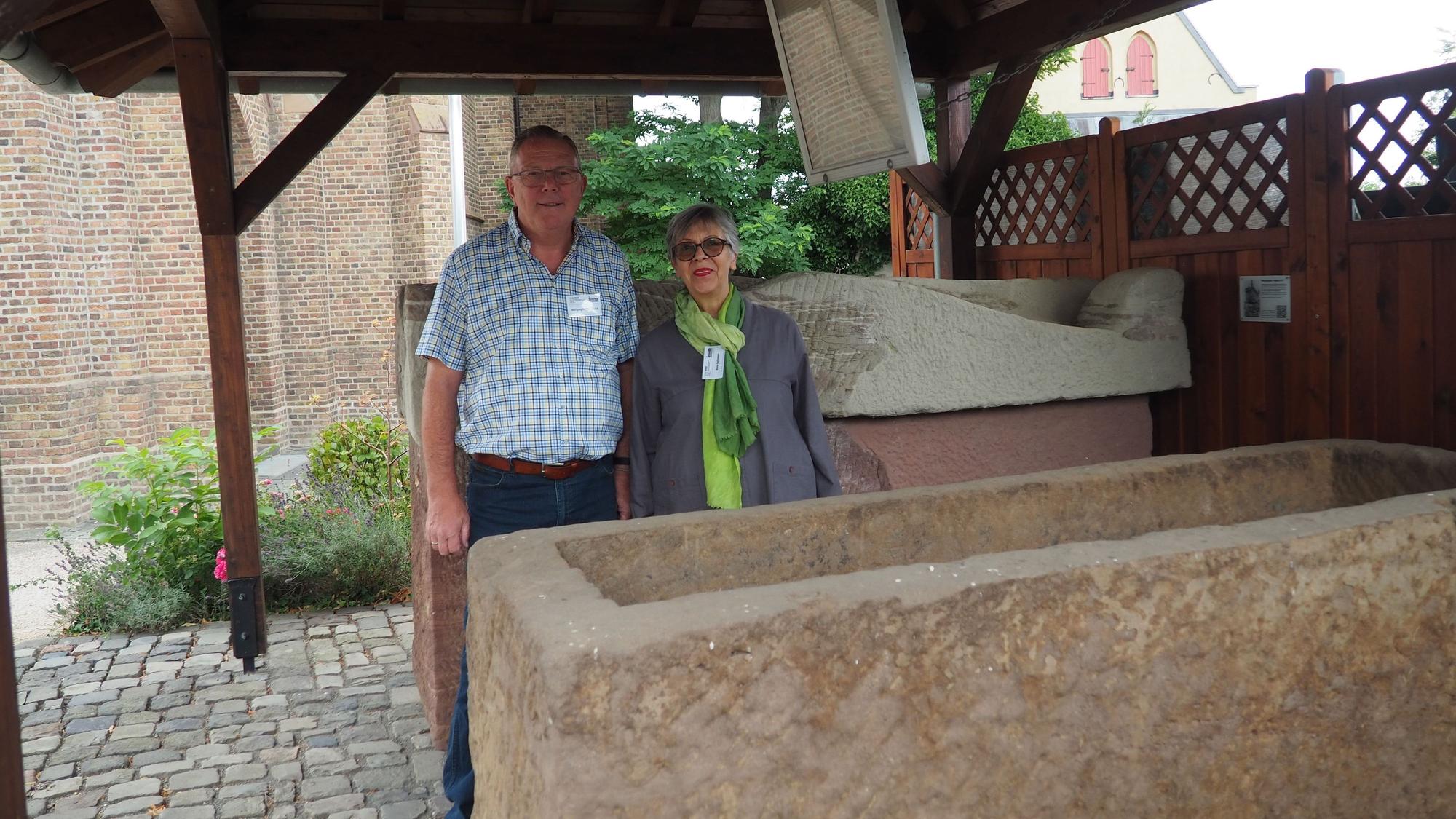 Ein Mann und eine Frau stehen zwischen zwei Steinsärgen.