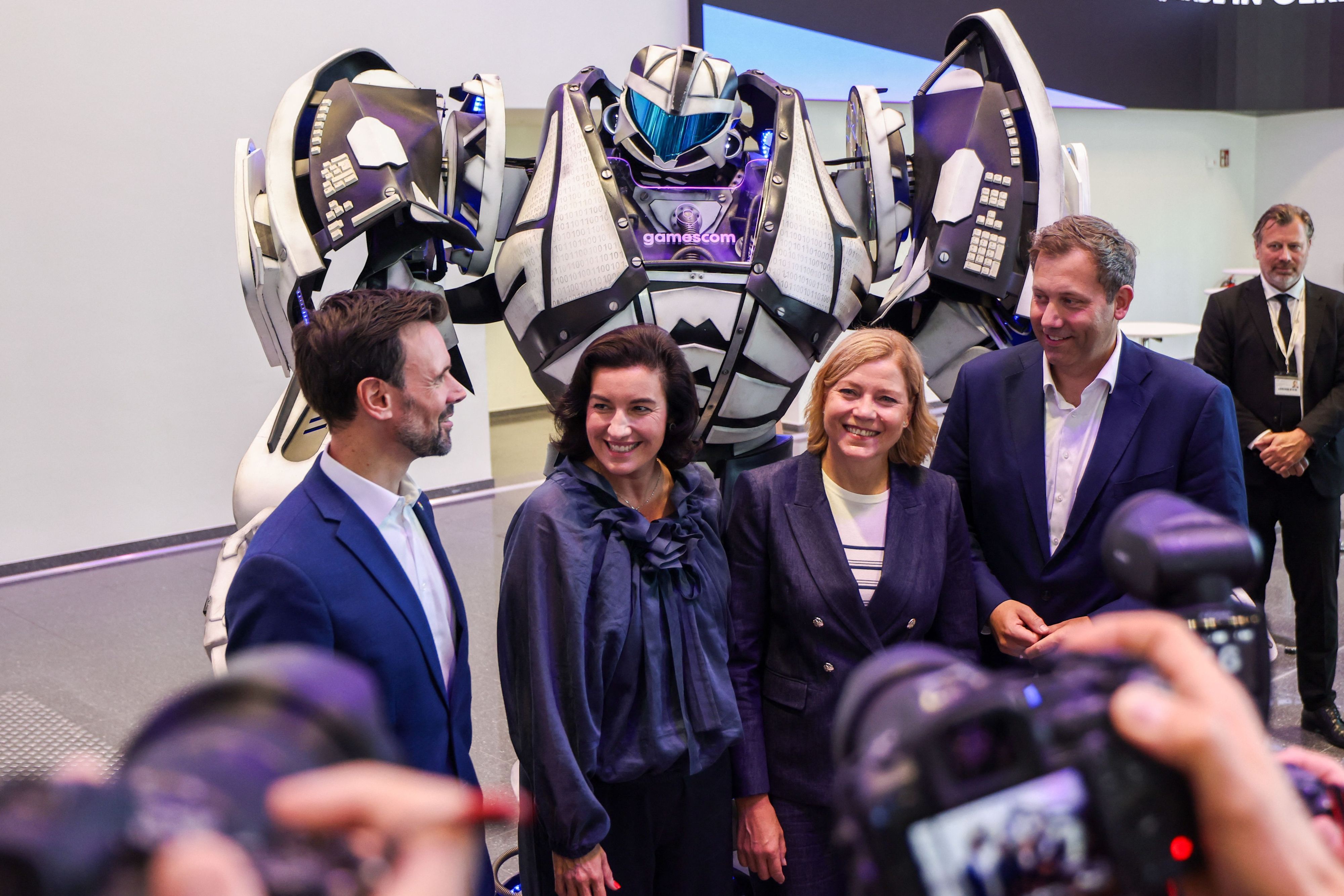 Felix Falk, Dorothee Bär, Henna Virkkunen und Lars Klingbeil stehen zur Eröffnung der Messe Gamescom vor einem Transformer-Roboter.