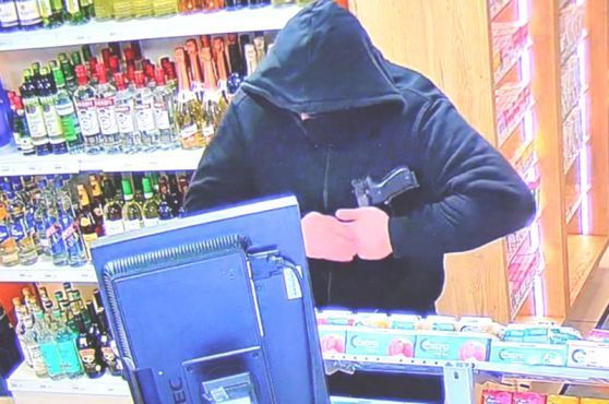 Auf dem Bild ist ein vermummter Mann an einer Tankstellenkasse zu sehen.