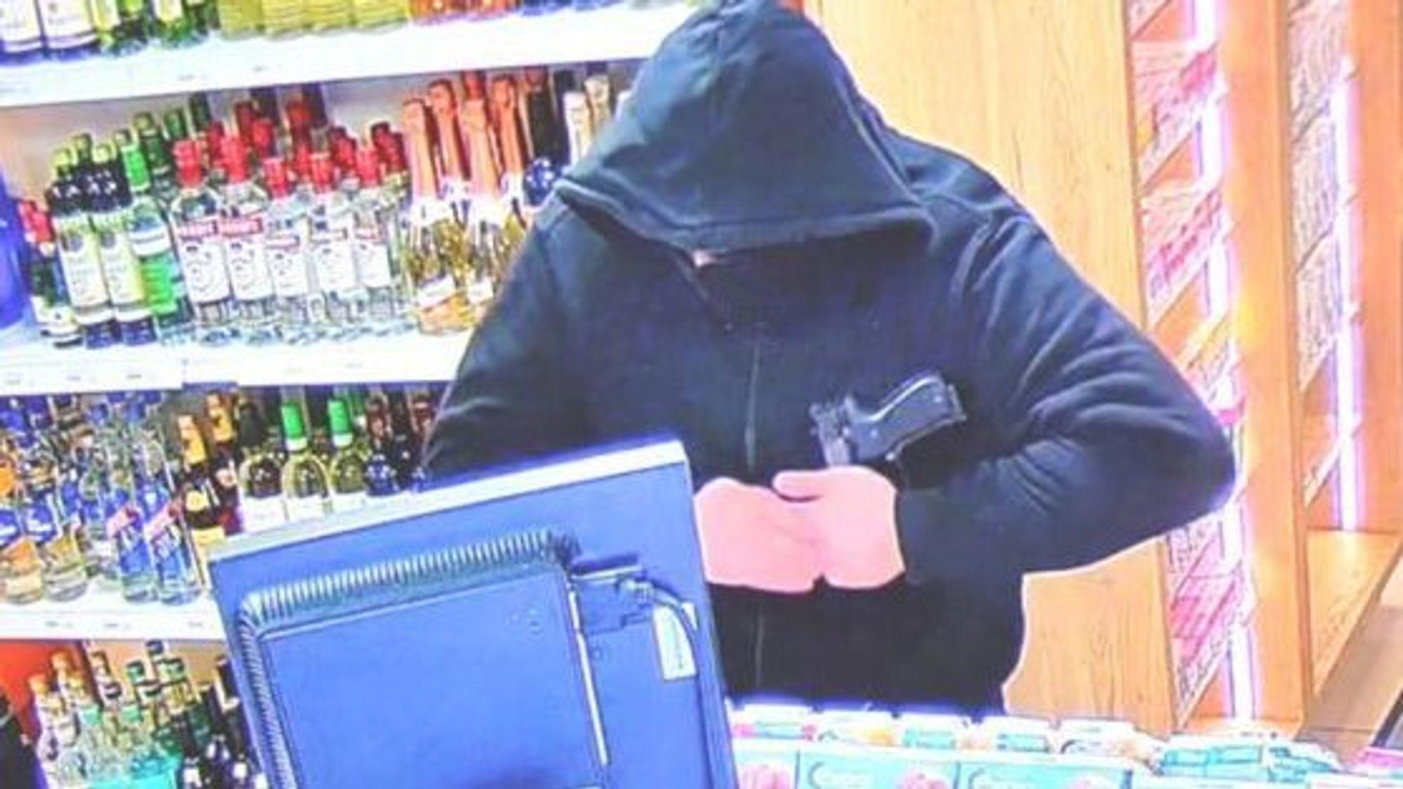 Auf dem Bild ist ein vermummter Mann an einer Tankstellenkasse zu sehen.