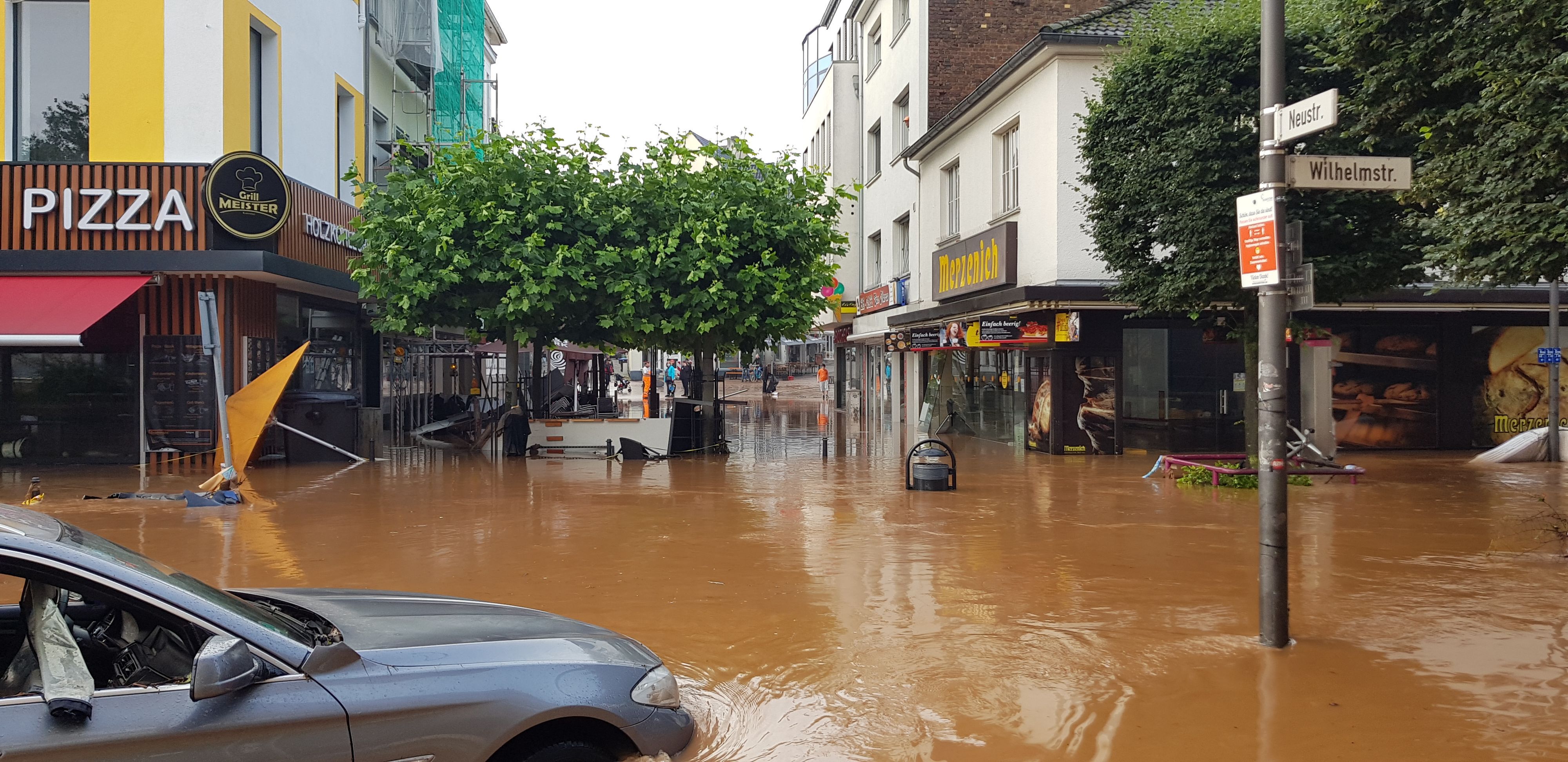 Das Wasser ist trüb-braun, ein Auto ist halb versunken, im Hintergund umgekipptes Gastronomie-Mobiliar.