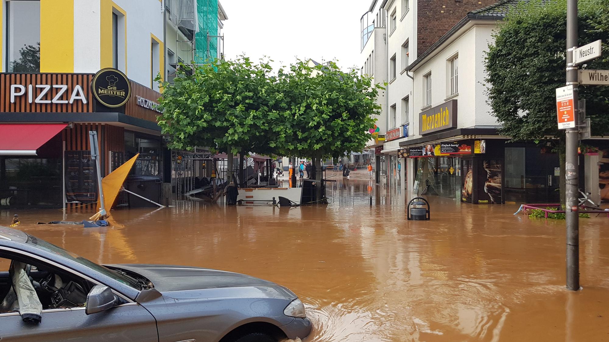 Das Wasser ist trüb-braun, ein Auto ist halb versunken, im Hintergund umgekipptes Gastronomie-Mobiliar.
