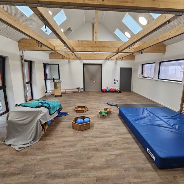Blick in die kleine Turnhalle mit einer großen blauen Matte, Klettergerüst und Bällen.