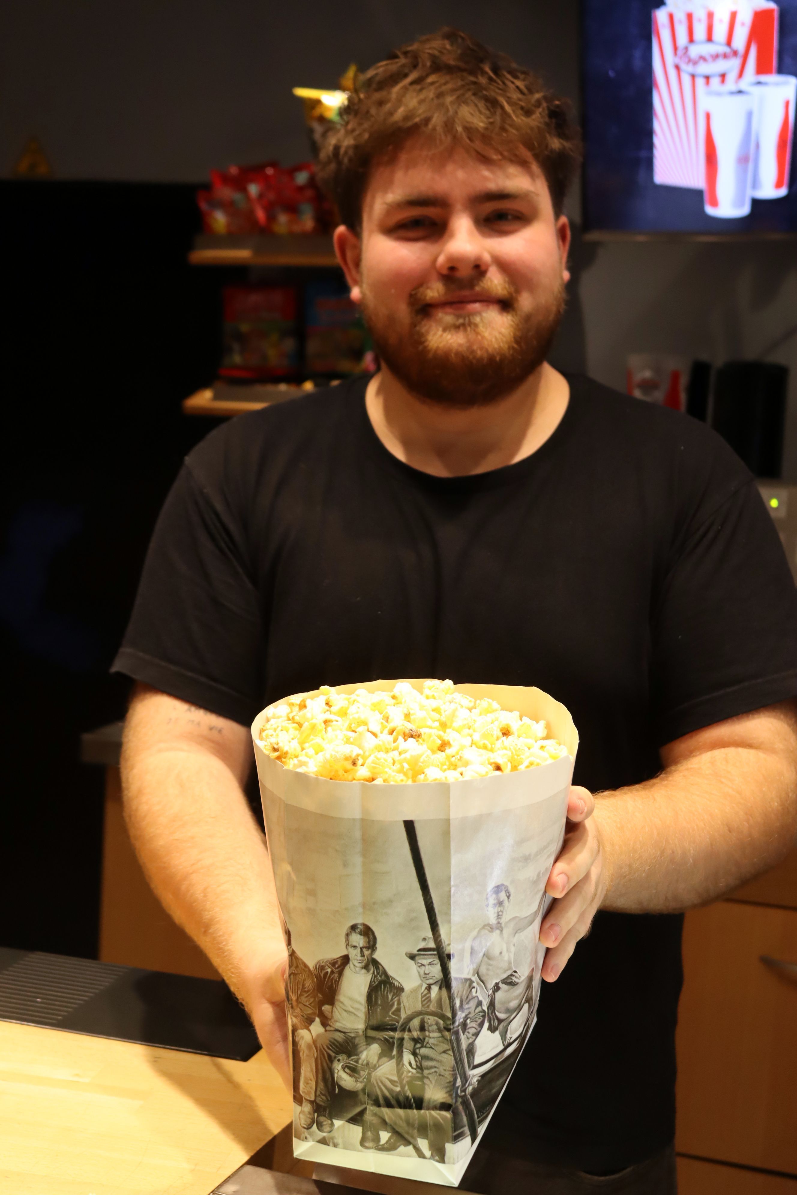 Ein Kinomitarbeiter hält eine Tüte Popcorn in den Händen.