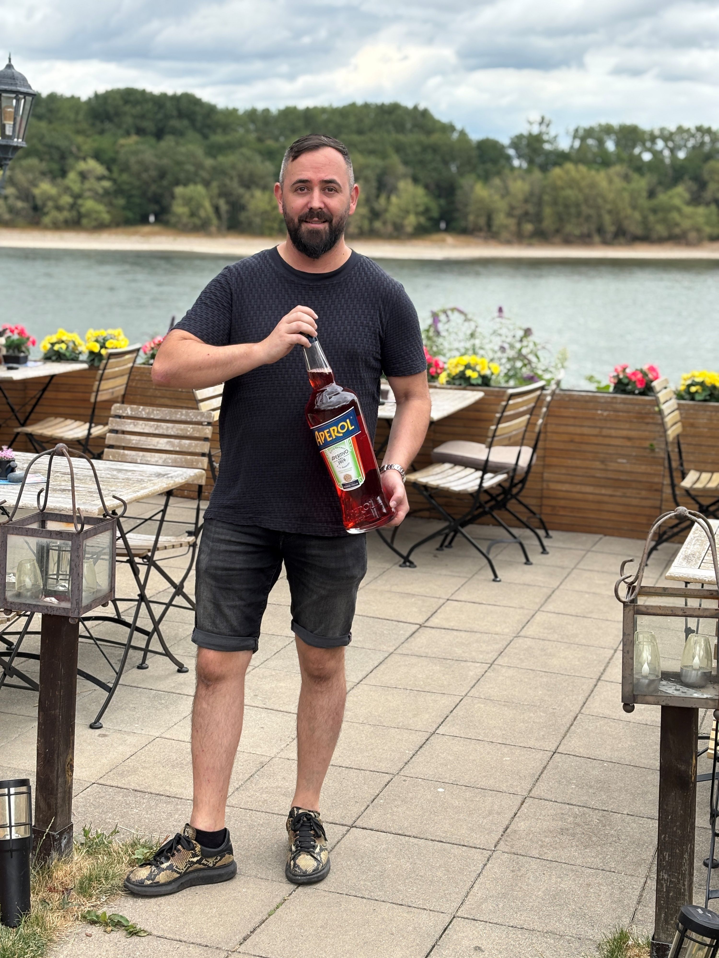 Auf dem Bild ist ein Mann zu sehen, der eine große Flasche Aperol in den Händen hält.
