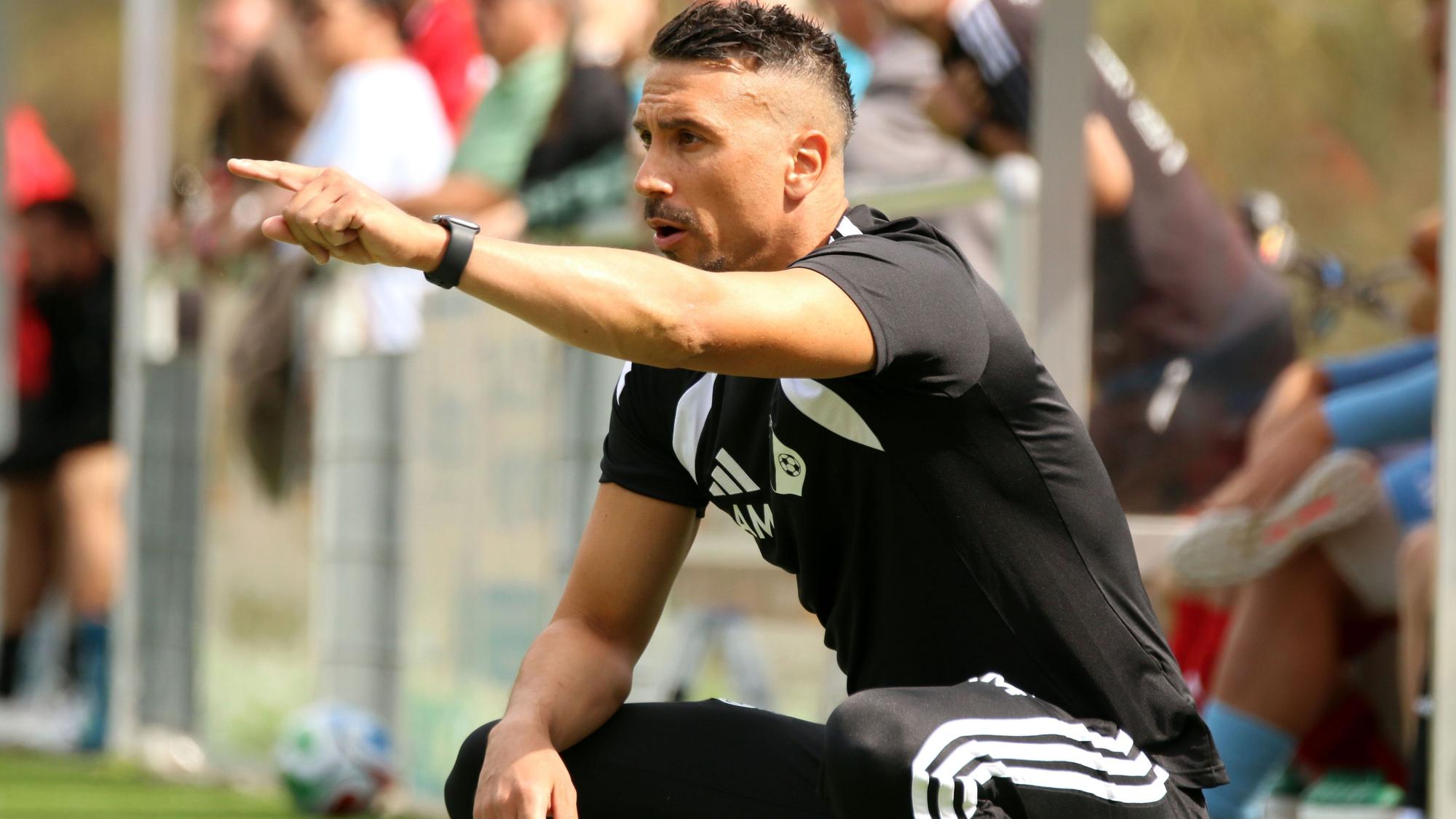 Angelo Mazza hockt neben dem Spielfeld und zeigt mit ausgestrecktem Zeigefinger etwas an.