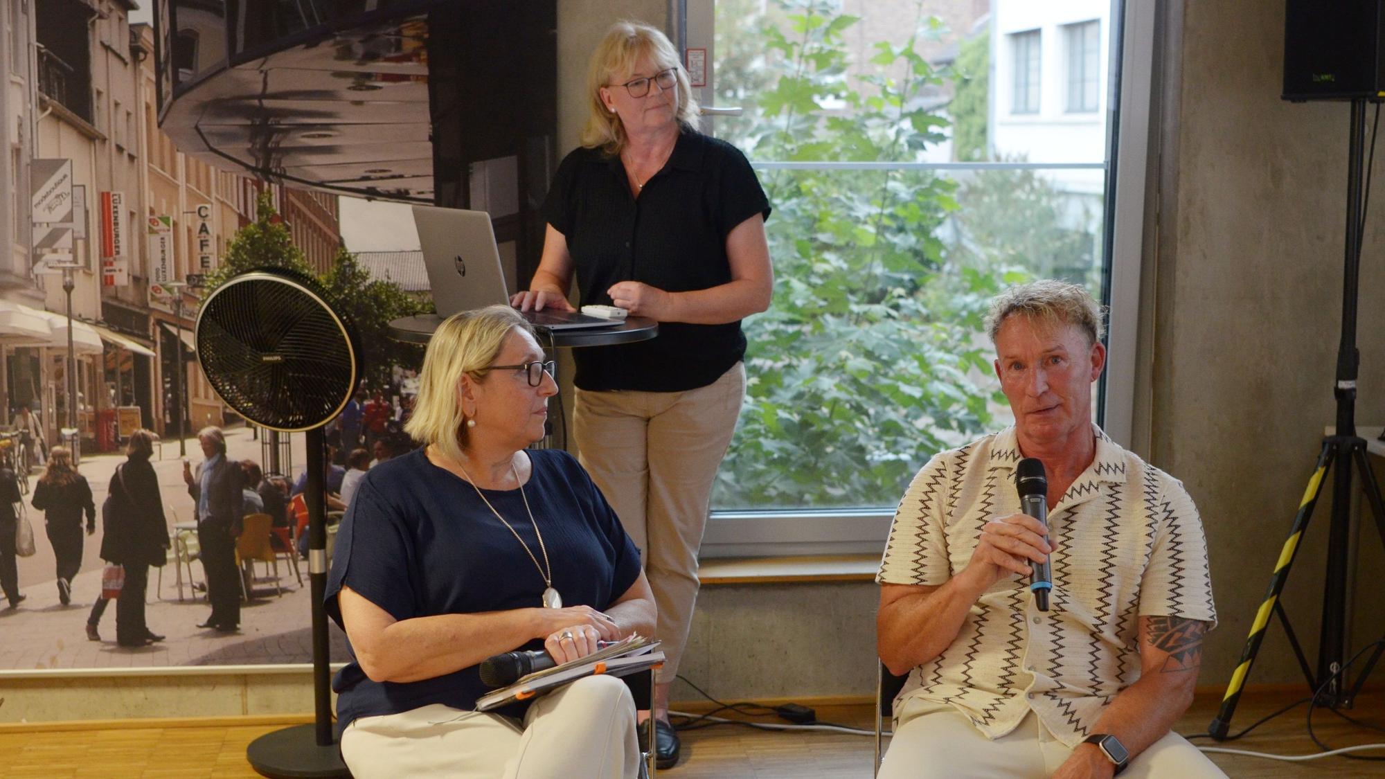 Die beiden Frauen schauen Gerres an, der in ein Mikrofon spricht.