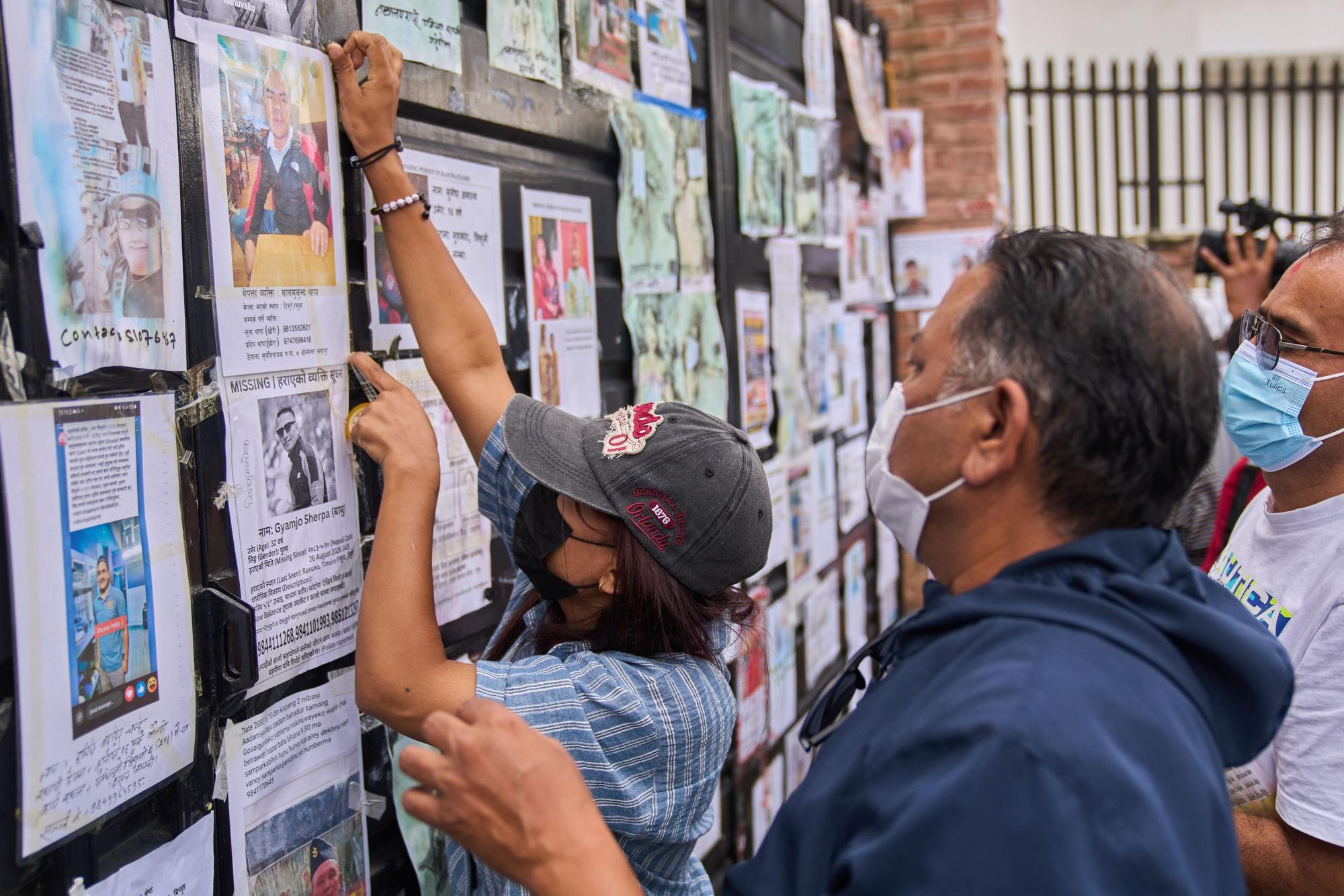 Eine Frau befestigt vor einem staatlichen Krankenhaus ein Foto eines vermissten Angehörigen an der Wand neben Fotos von vermissten und verstorbenen Personen.