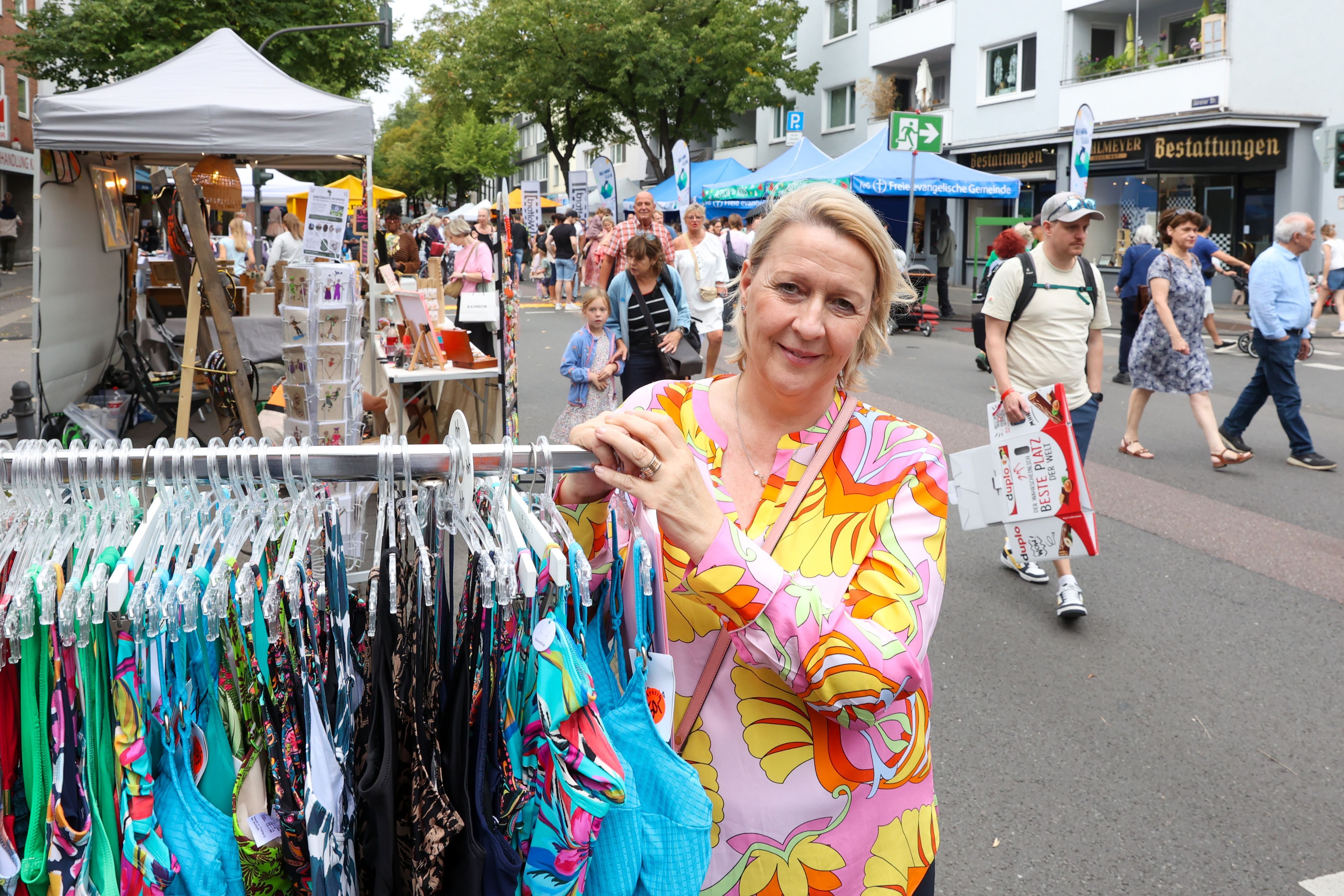 Eine Frau im bunten Kleid steht neben einem Ständer mit Bademoden.