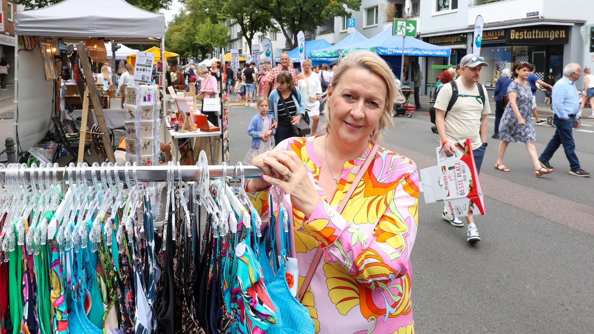 Eine Frau im bunten Kleid steht neben einem Ständer mit Bademoden.