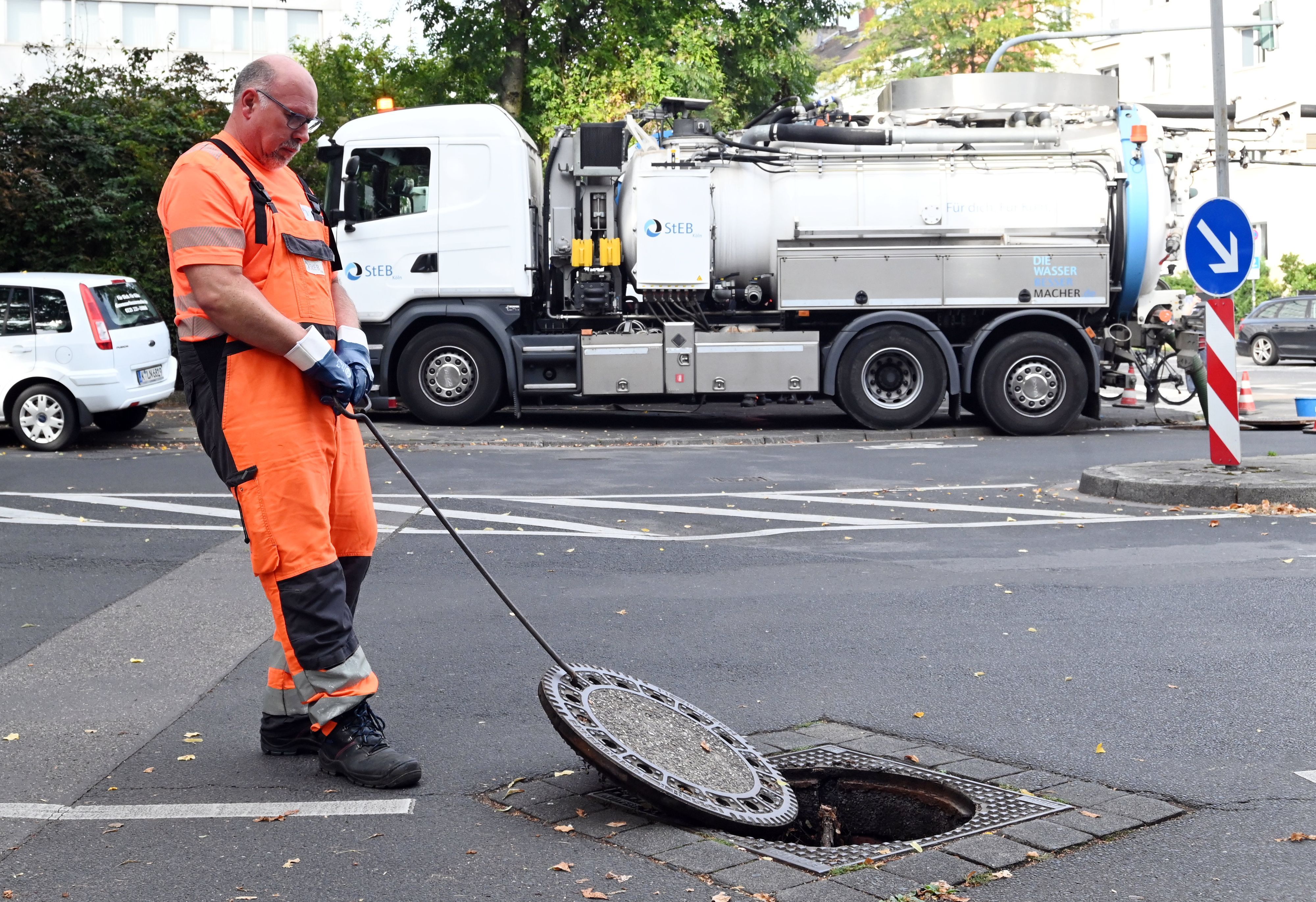 Ein Mann im orangefarbenen Anzug öffnet einen Kanaldeckel
