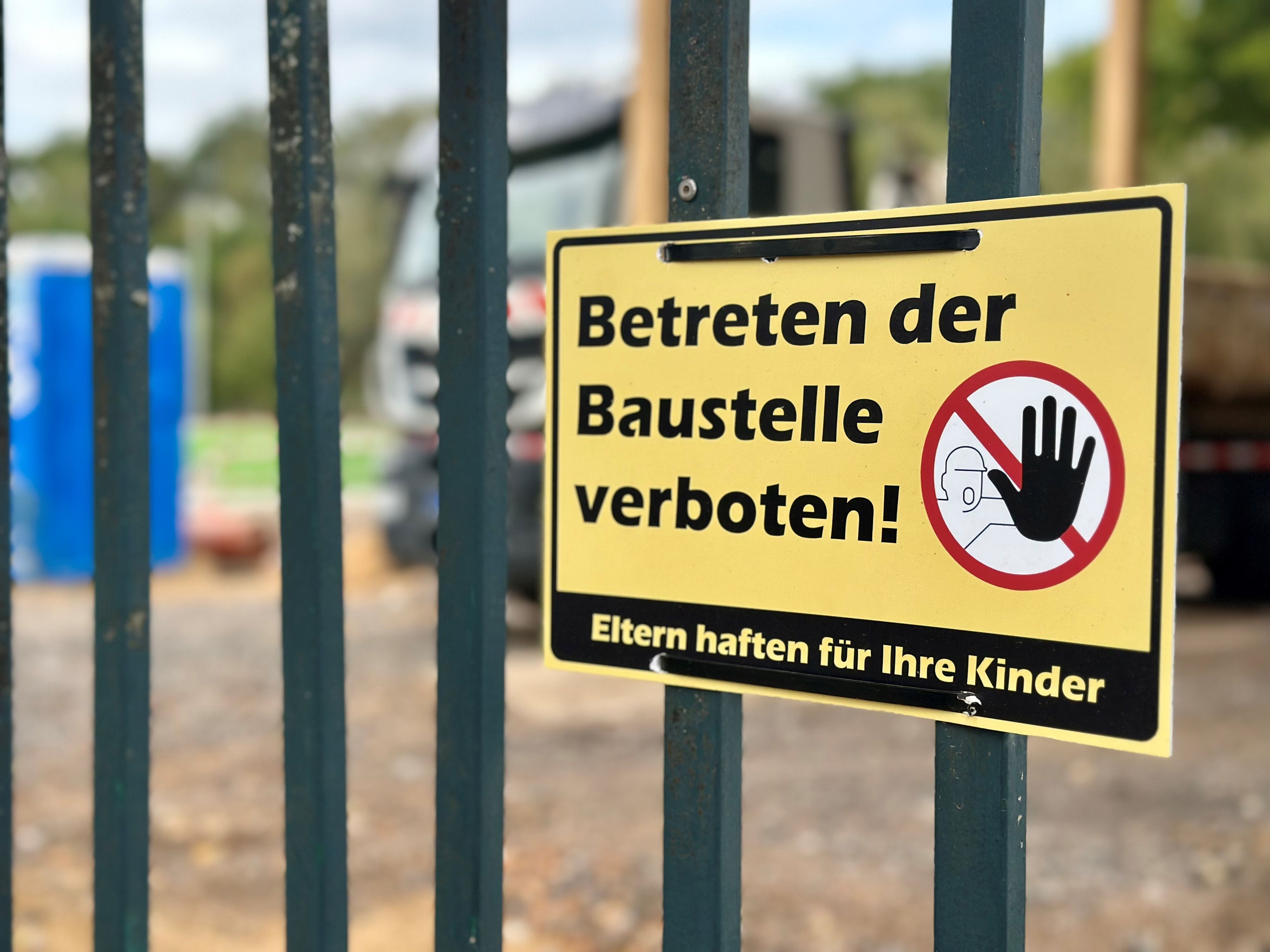 Ein gelbes Schild mit der Aufschrift „Betreten der Baustelle verboten“ hängt an einem Zaun.