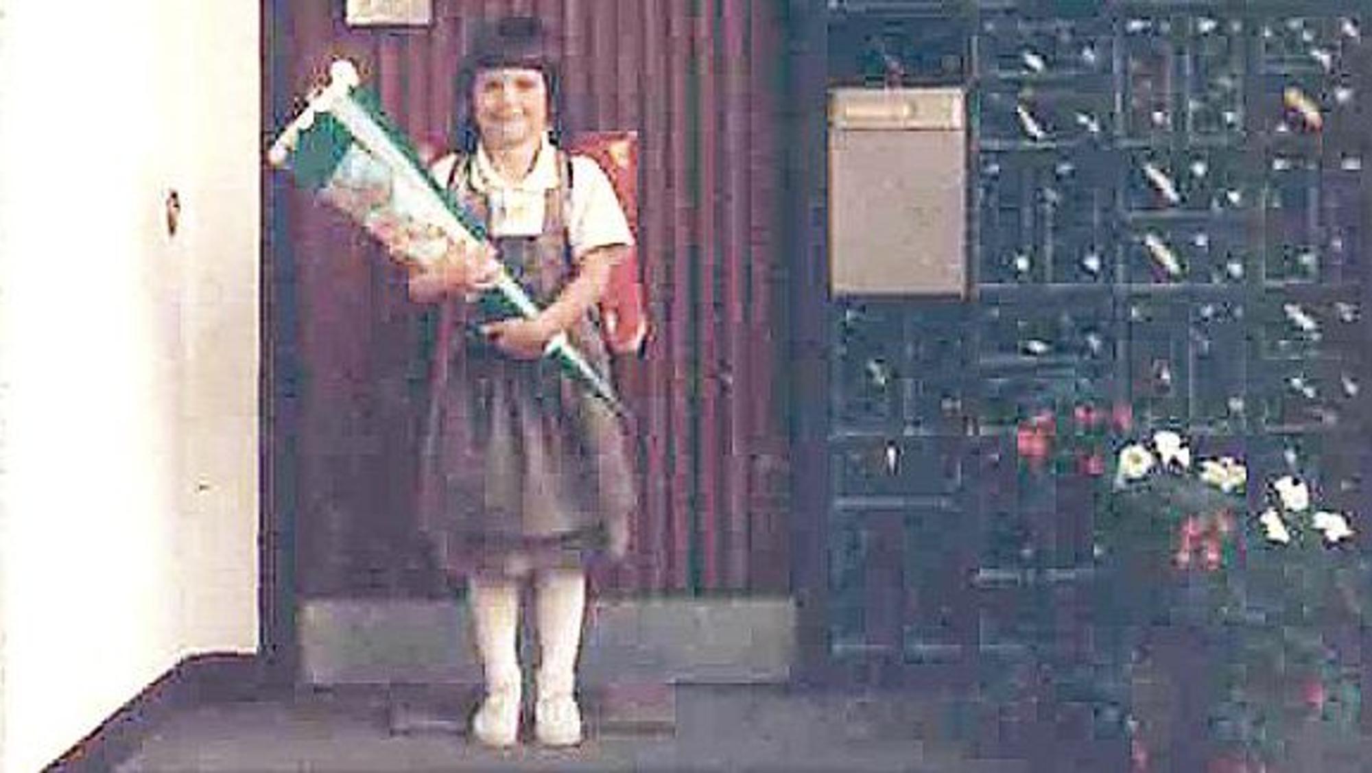 Ein Mädchen mit Schultüte und Ranzen steht vor einem Haus.