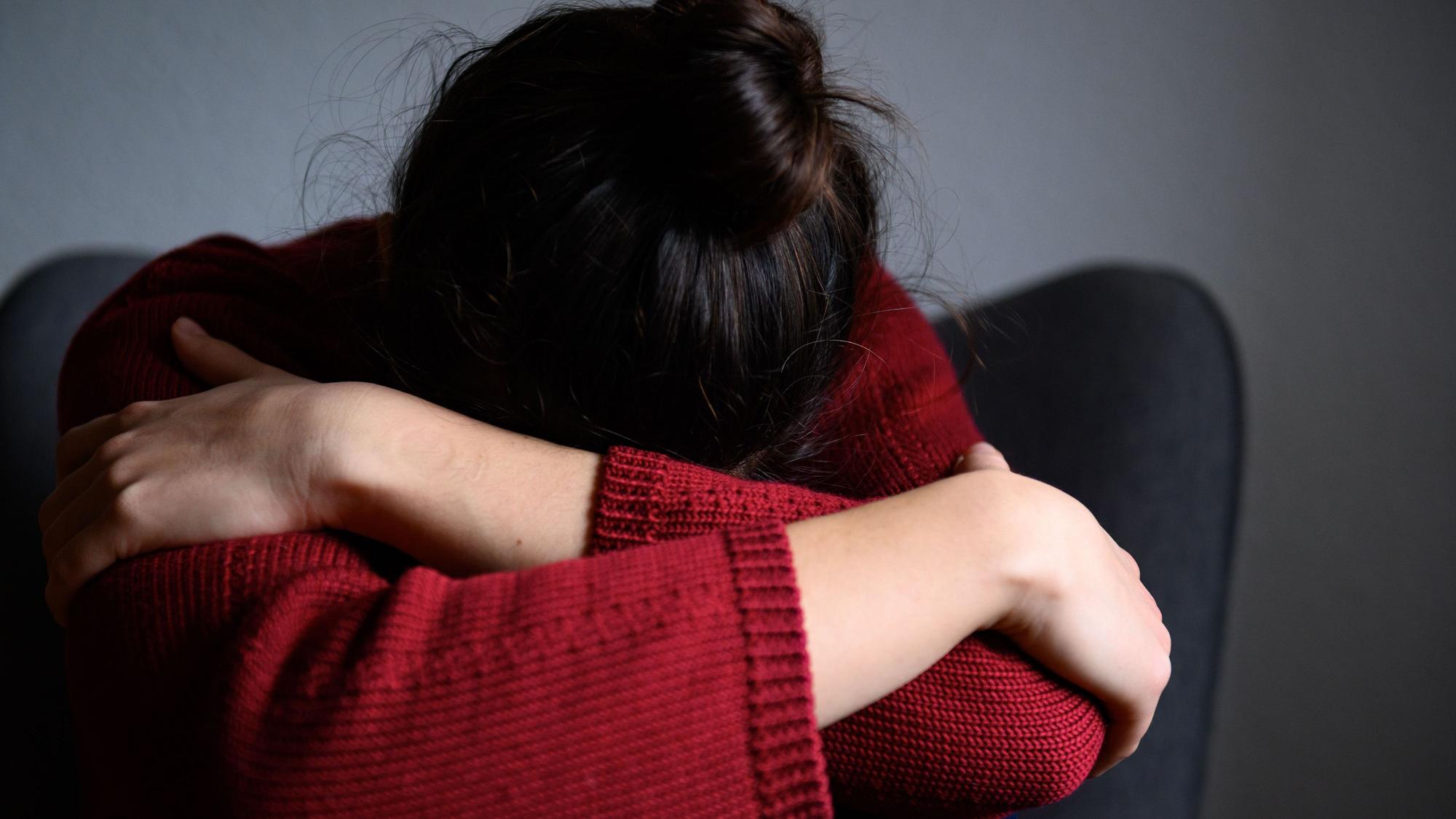 Eine Frau sitzt mit dem Kopf in den Armen versunken auf einem Stuhl.