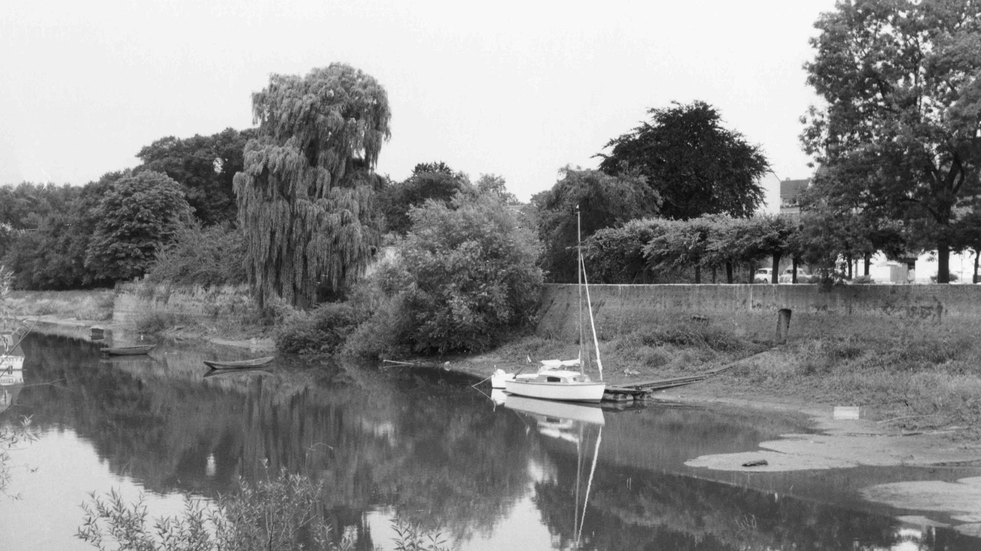 Historisches Schwarz-Weiß-Bild: Am toten Rheinarm gab es keine Anlegestelle, Boote mussten über eine Kuhweide bis zu einer schmalen Wasserverbindung zum Rhein getragen werden. Später entstand hier der Hafen.