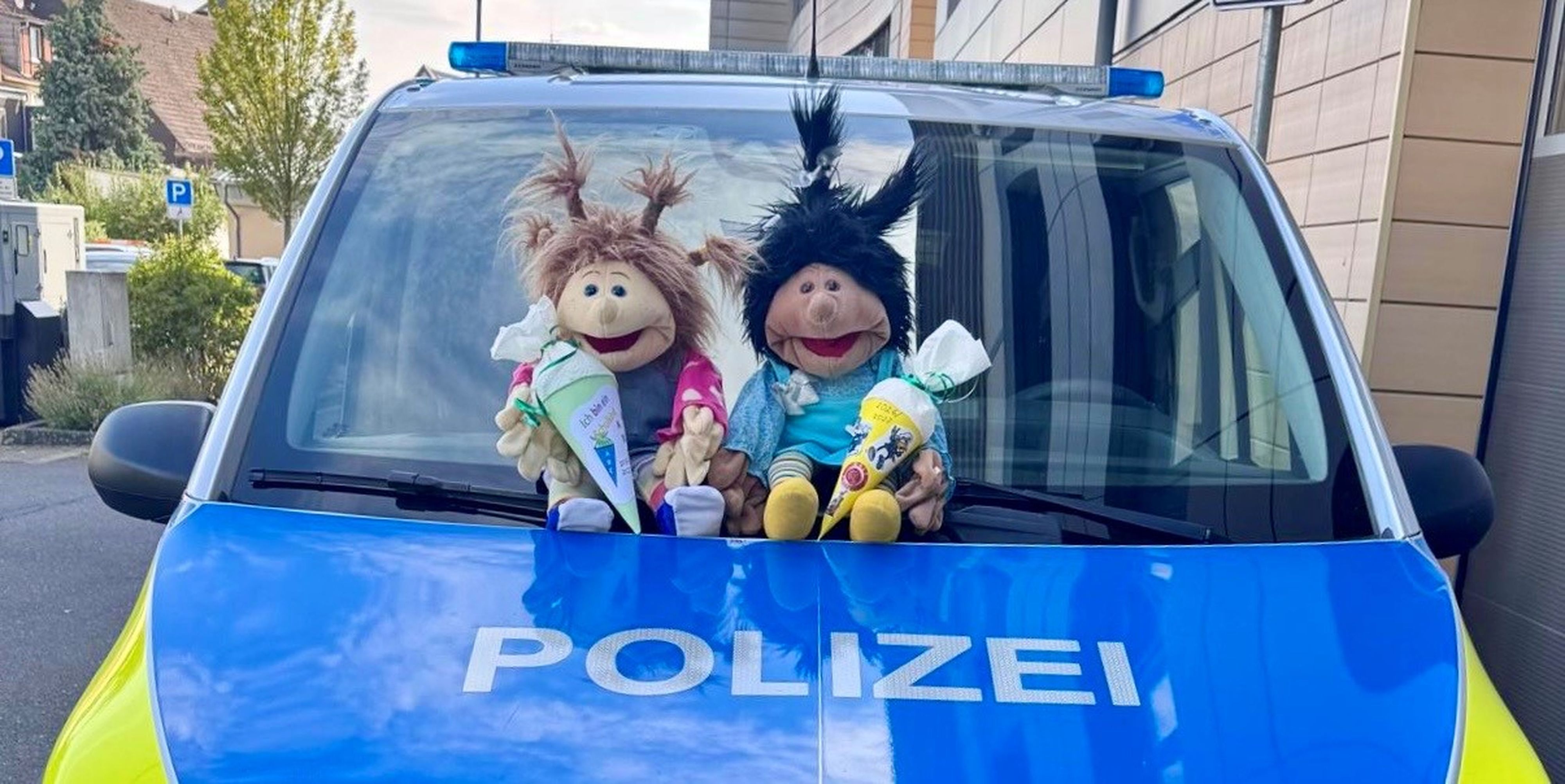 Zwei Stofffiguren sitzen vor der Windschutzscheibe eines Polizeiwagens.