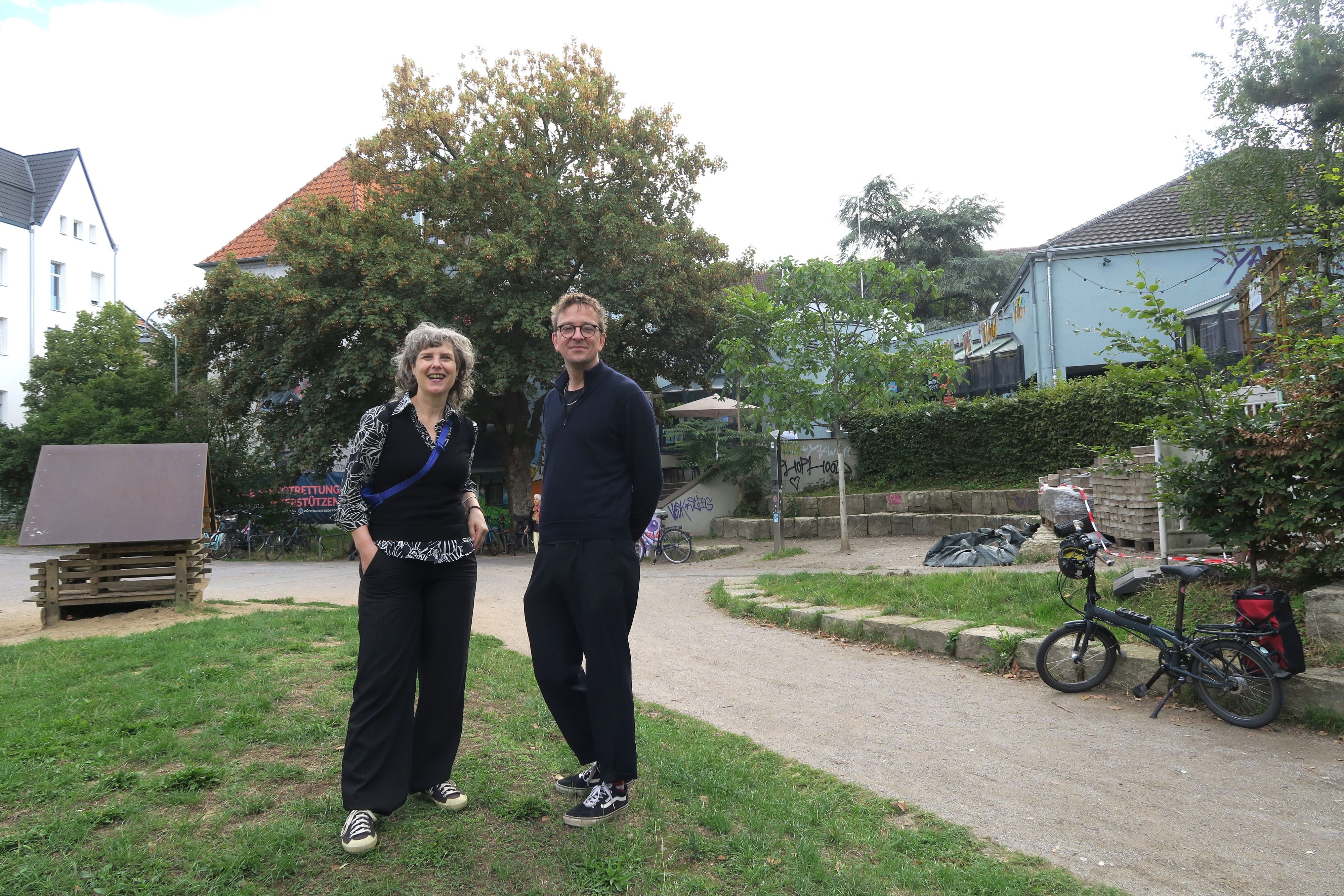 Eine Frau und ein Mann stehen nebeneinander in einem Park vor dem Bürgerzentrum Ehrenfeld.