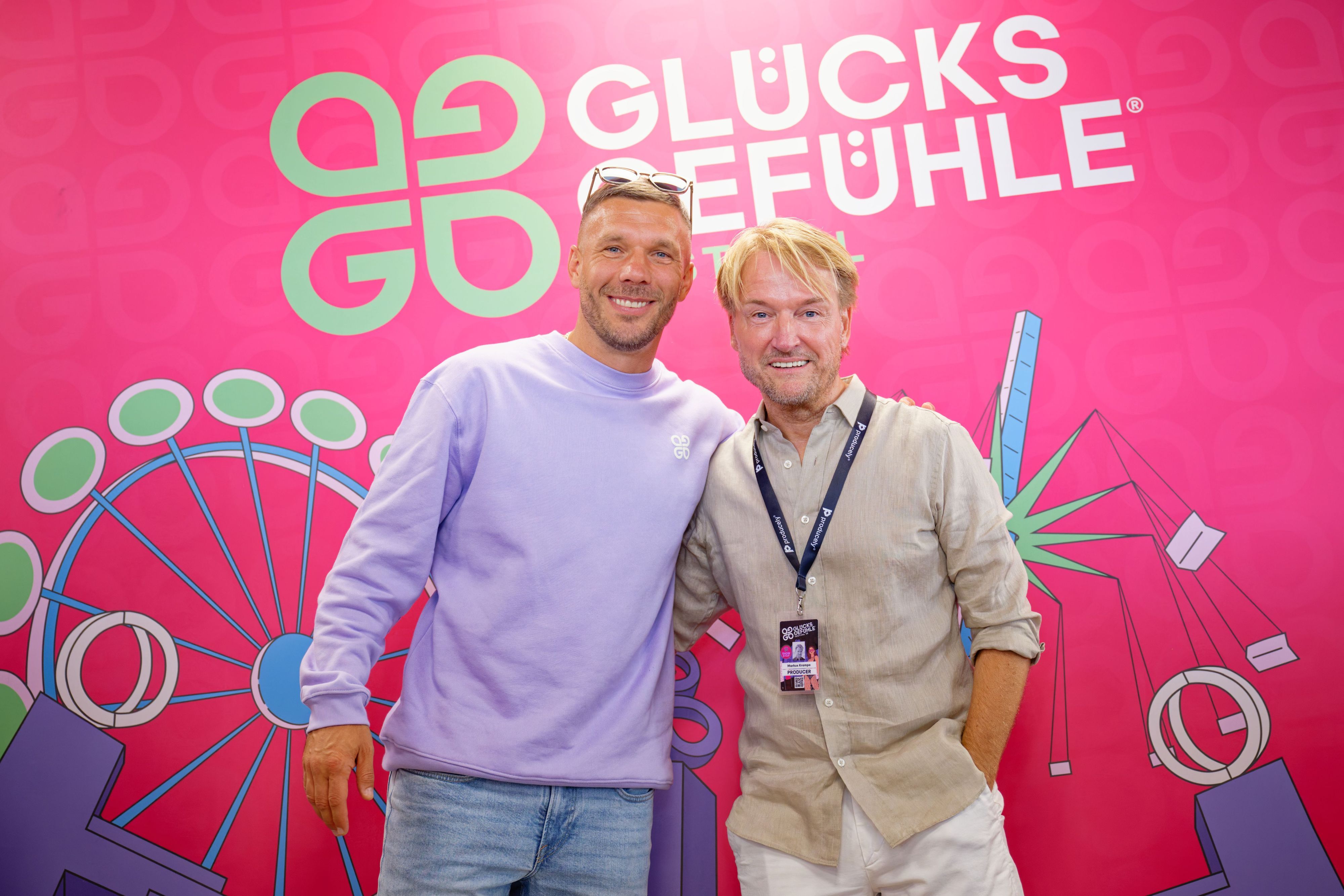 Der Fußballspieler Lukas Podolski (l.) und Musikmanager Markus Krampe stehen auf dem Hockenheimring während einer Pressekonferenz vor einem Logo des Glücksgefühle-Festivals. (Archivbild)