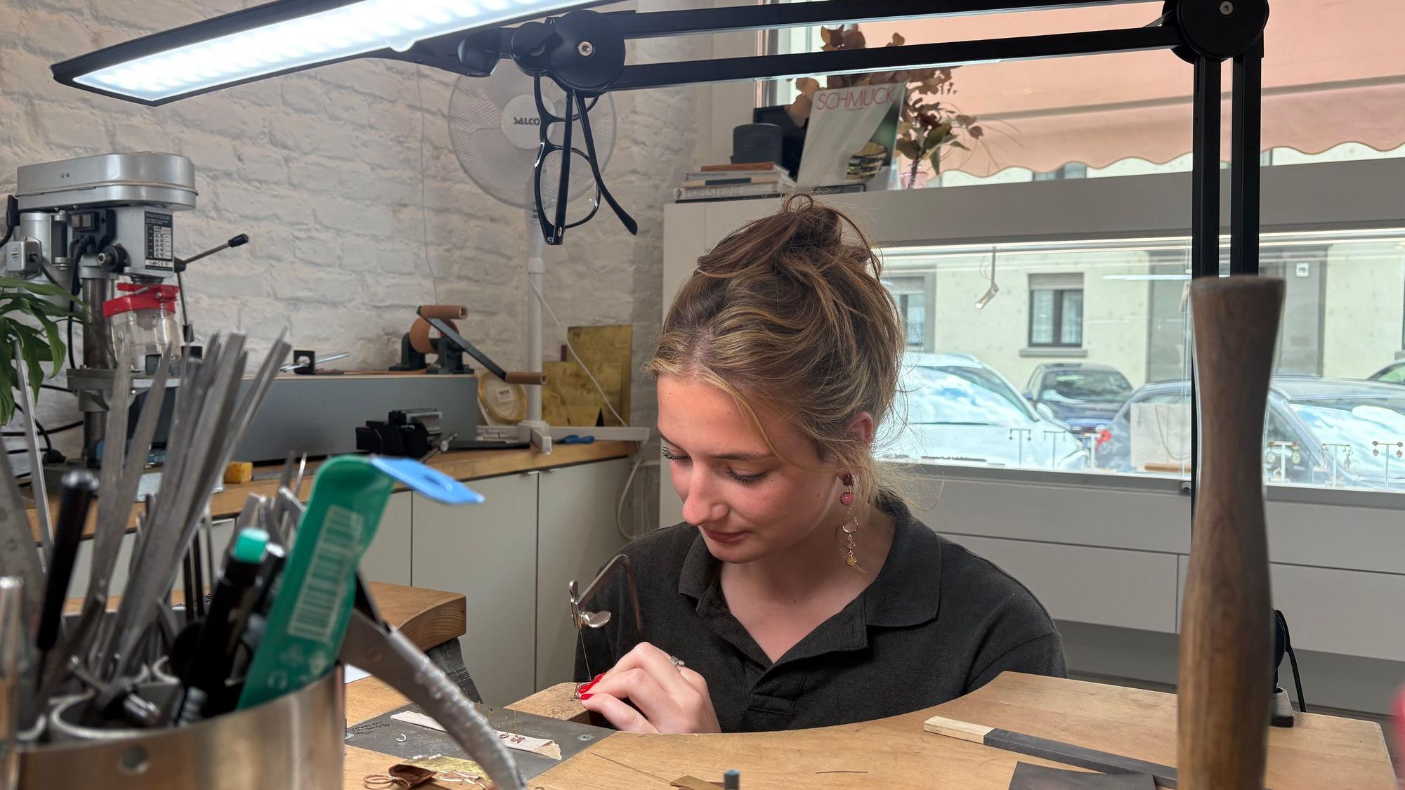 Elisabeth sitzt an ihrem Werkbrett und sägt ein Modell.