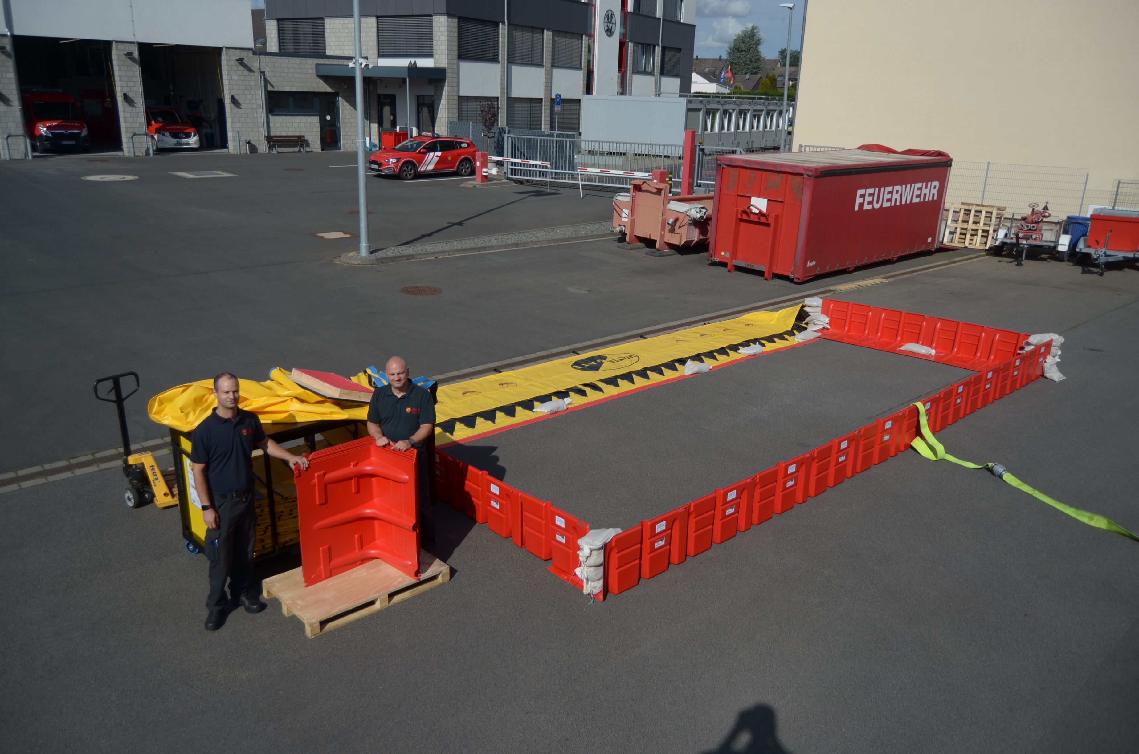 Die beiden Feuerwehrmänner stehen auf dem Betriebshof der Feuerwehr neben den Sperrsystemen.
