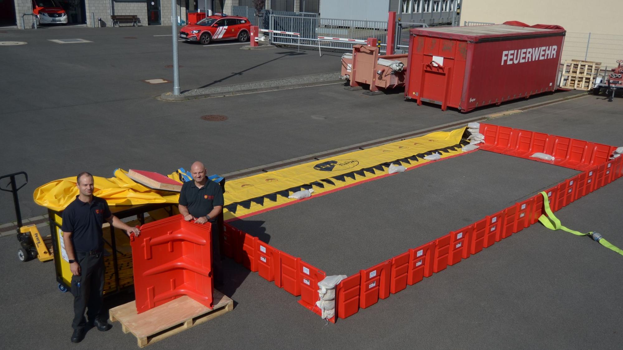 Die beiden Feuerwehrmänner stehen auf dem Betriebshof der Feuerwehr neben den Sperrsystemen.
