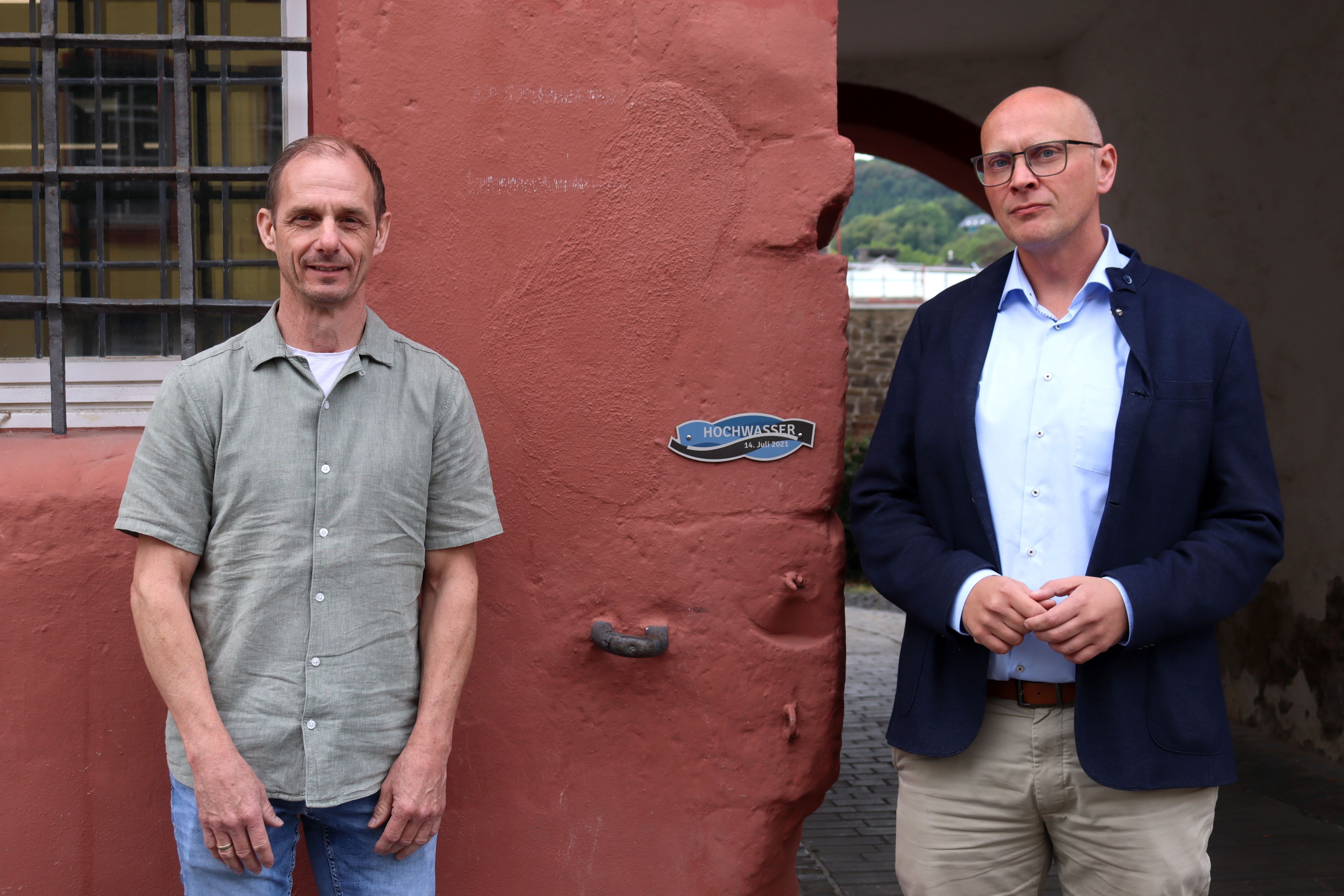 Bad Münstereifels Bürgermeister Sebastian Glatzel und Ralf Wassong stehen an der Flutmarke, die am Rathaus angebracht ist.