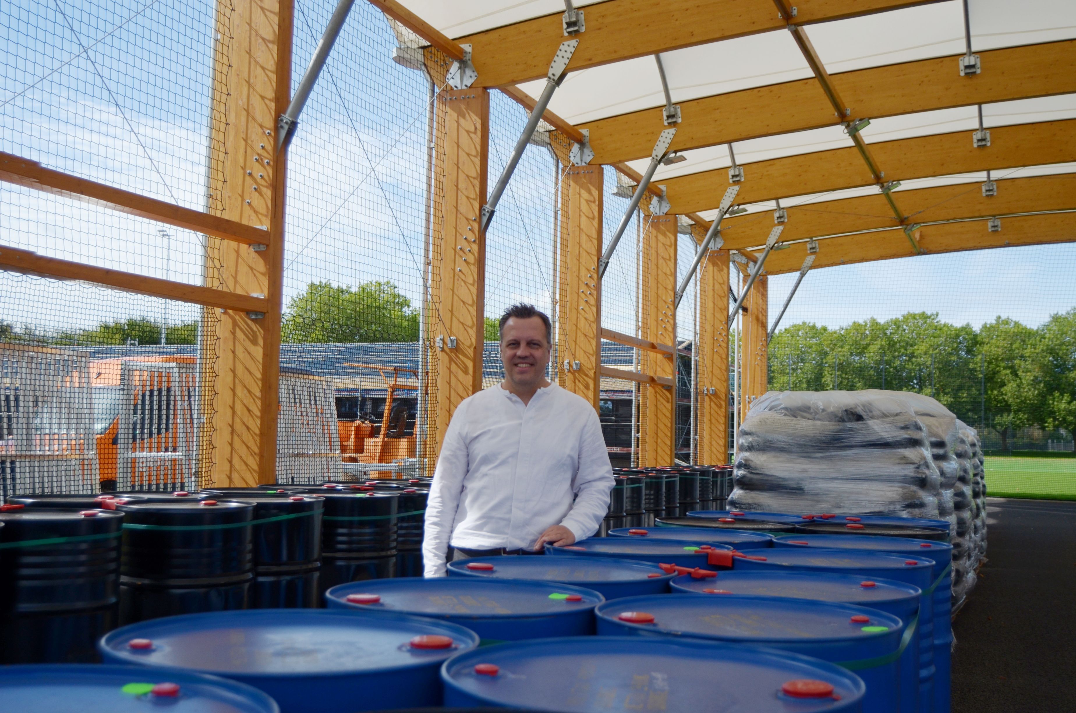 Sacha Reichelt stützt sich auf einen blauen Behälter. Im Hintergrund steht das neue Umkleidegebäude.