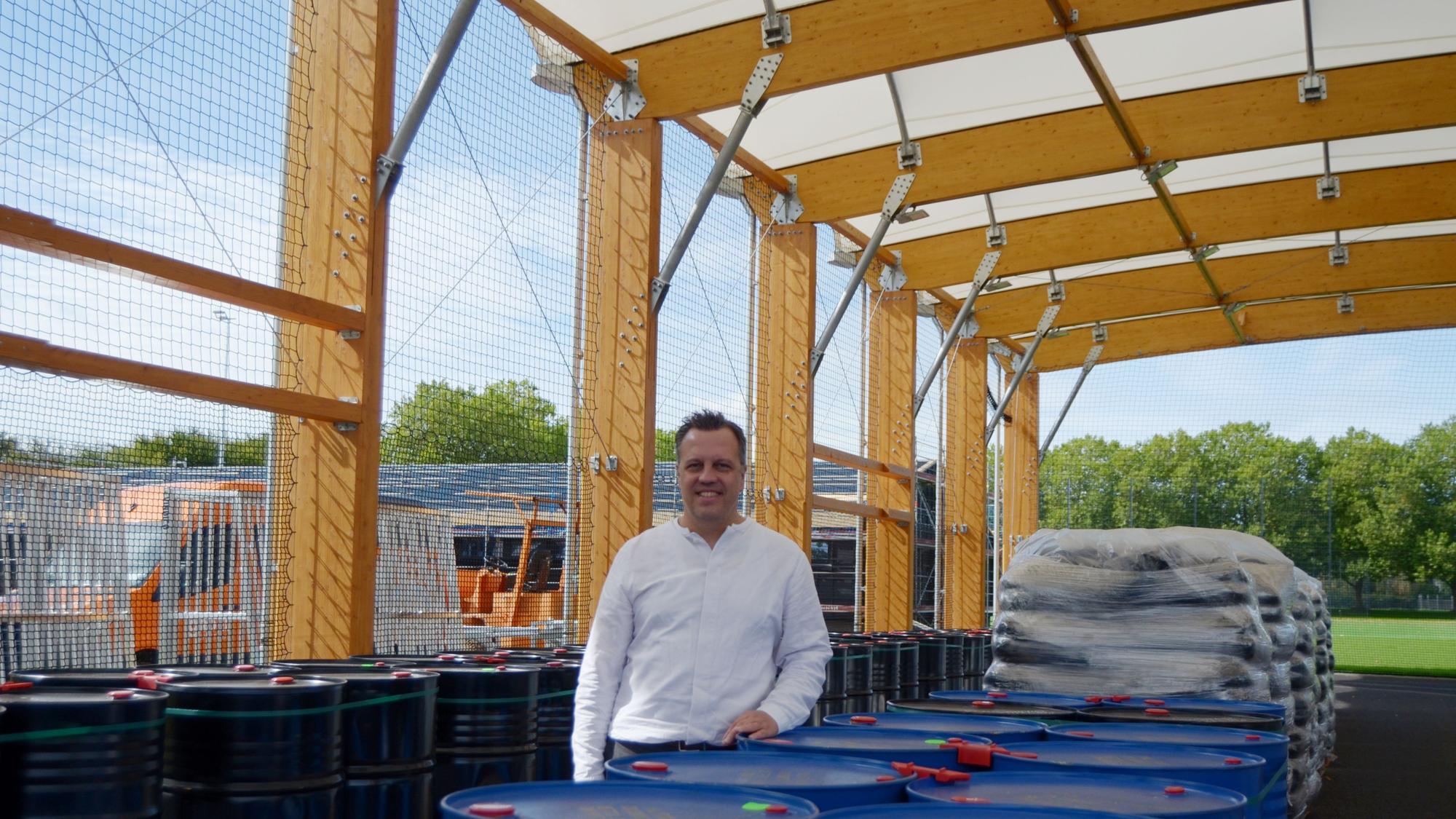 Sacha Reichelt stützt sich auf einen blauen Behälter. Im Hintergrund steht das neue Umkleidegebäude.