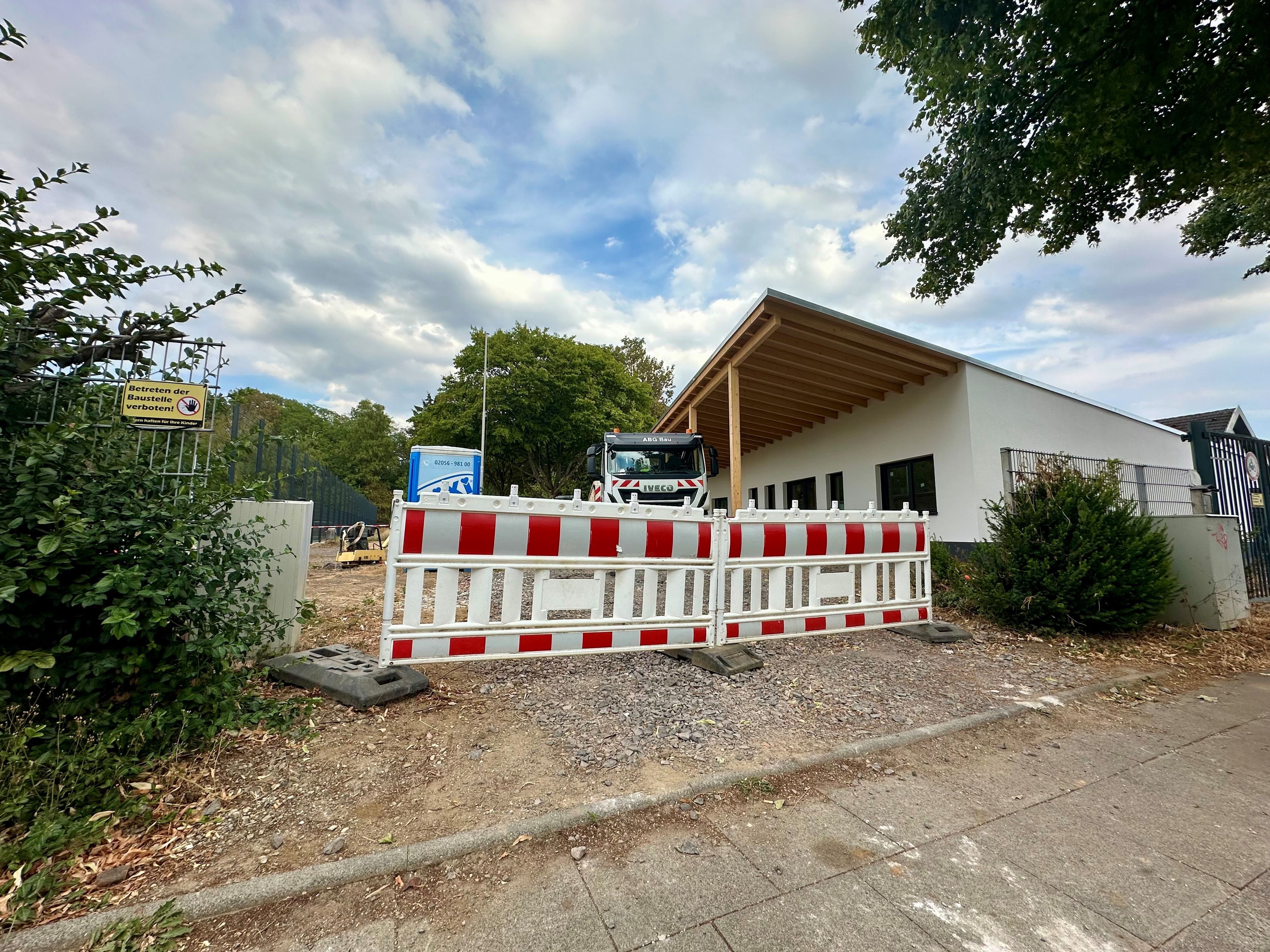Baustellenbaken stehen vor einem Sportplatz mit Sportlerheim.