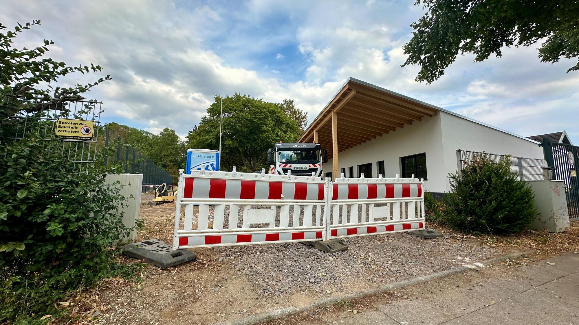 Baustellenbaken stehen vor einem Sportplatz mit Sportlerheim.