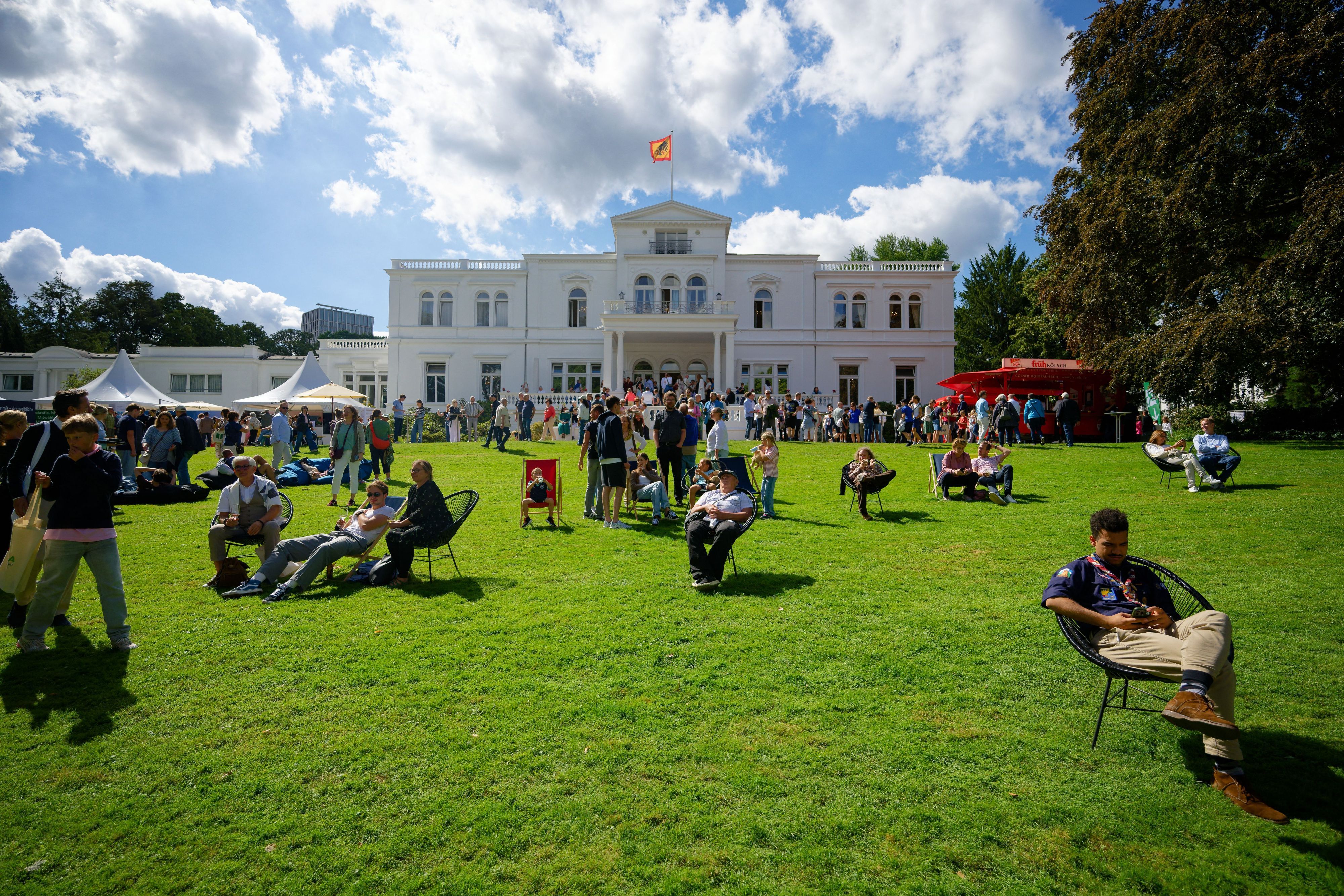 Besucher sitzen beim Bürgerfest im Park der Villa Hammerschmidt auf dem Rasen vor dem Bonner Amtssitz des Bundespräsidenten.