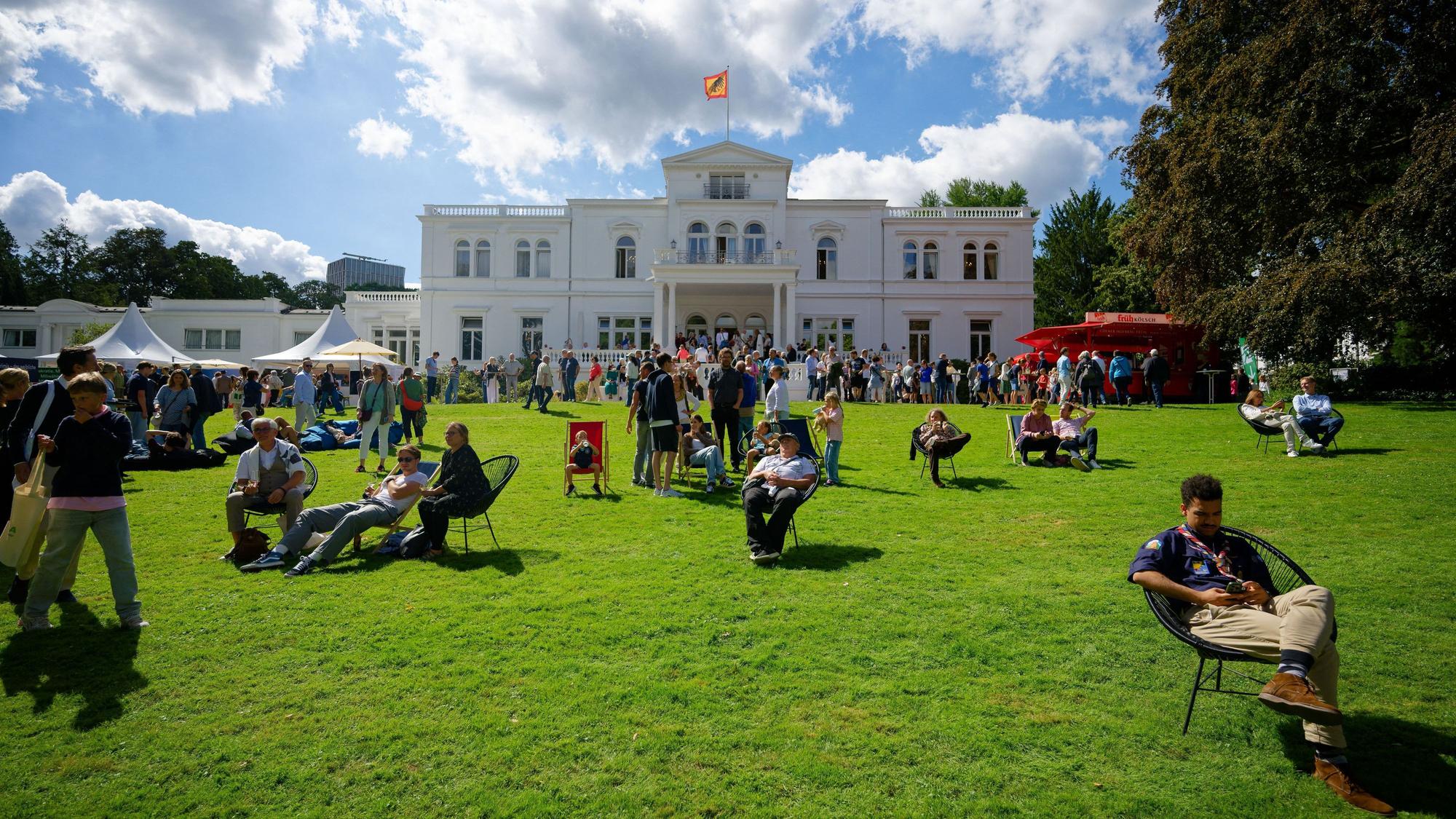 Besucher sitzen beim Bürgerfest im Park der Villa Hammerschmidt auf dem Rasen vor dem Bonner Amtssitz des Bundespräsidenten.