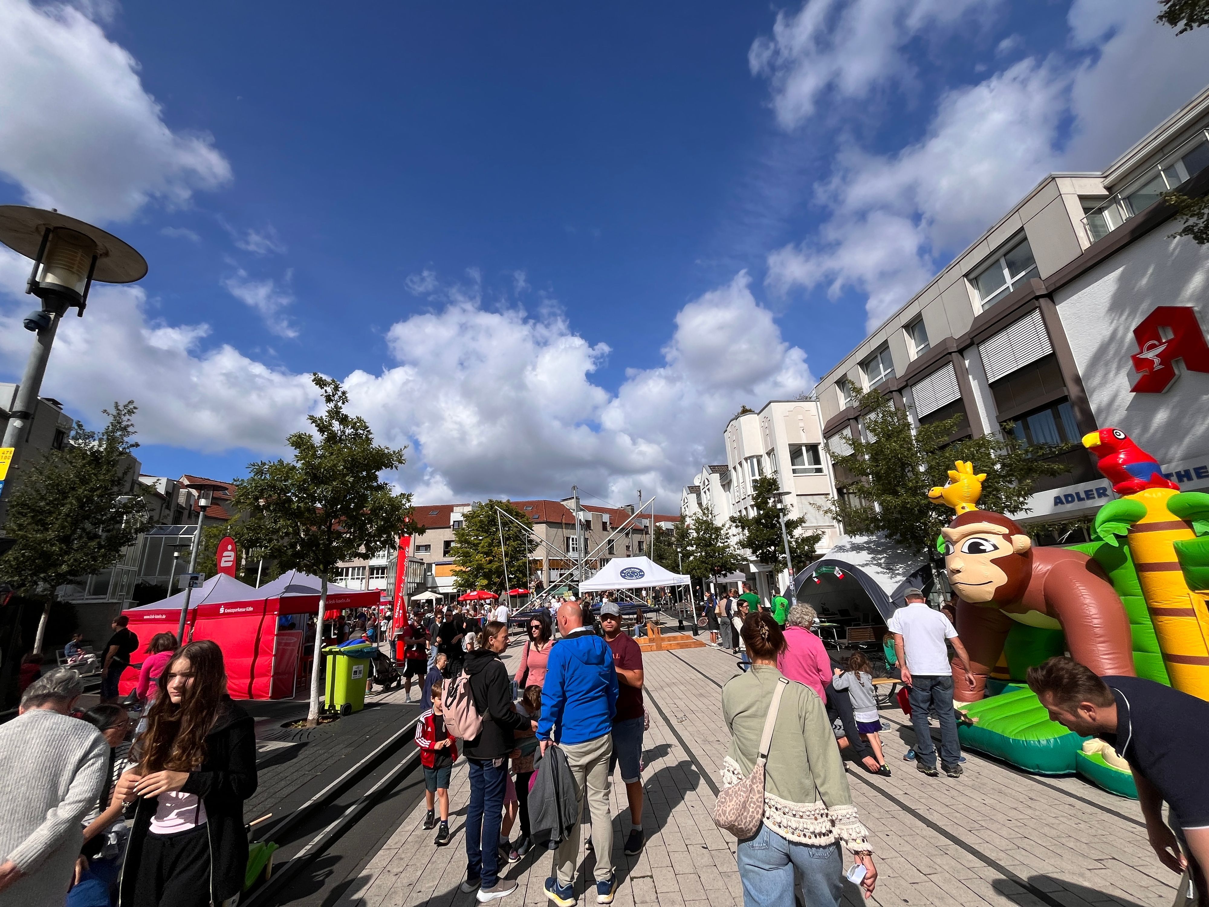 Viele Menschen und Stände auf einem Platz, rechts steht eine Hüpfburg.