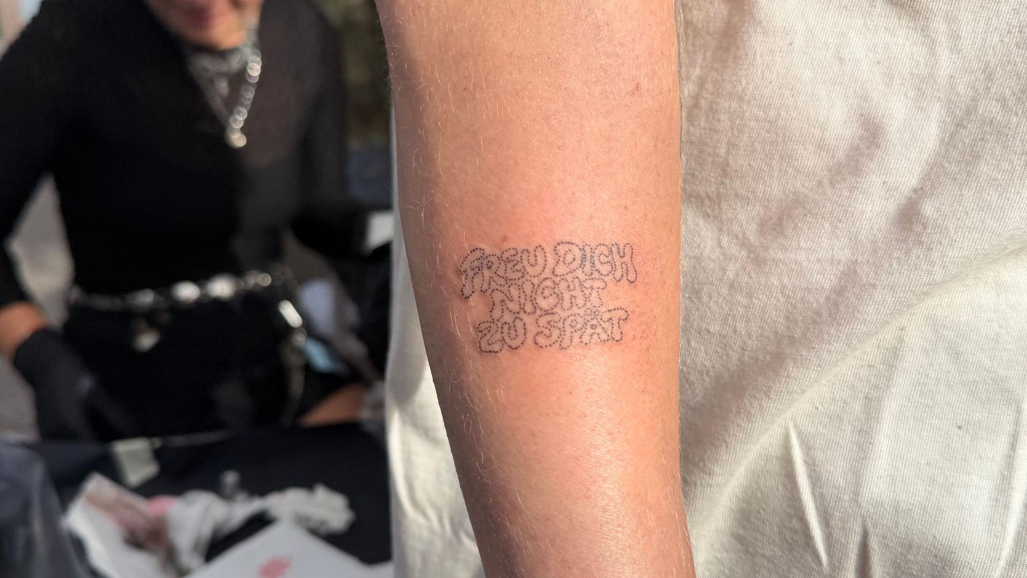 Ein Arm auf dem die Worte „Freu dich nicht zu spät“ tätowiert sind.