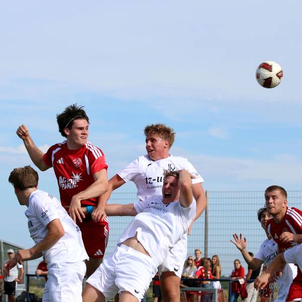 Ein Zülpicher Spieler im roten Trikot steigt gegen drei Siegburger in Weiß zum Kopfball hoch, ein Siegburger schreit offensichtlich vor Schmerzen.