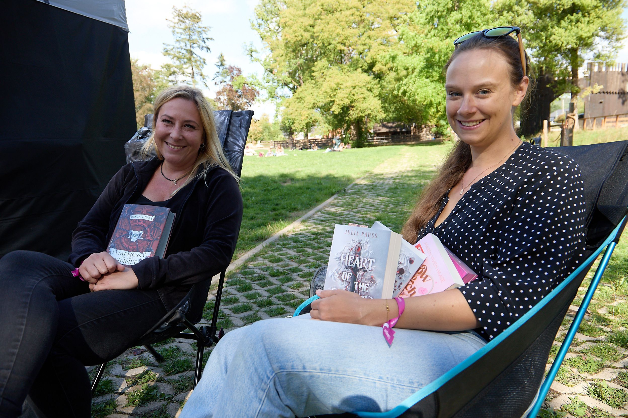 Zwei Frauen sitzen in Klappstühlen auf einer Wiese. Sie halten Bücher in den Händen.