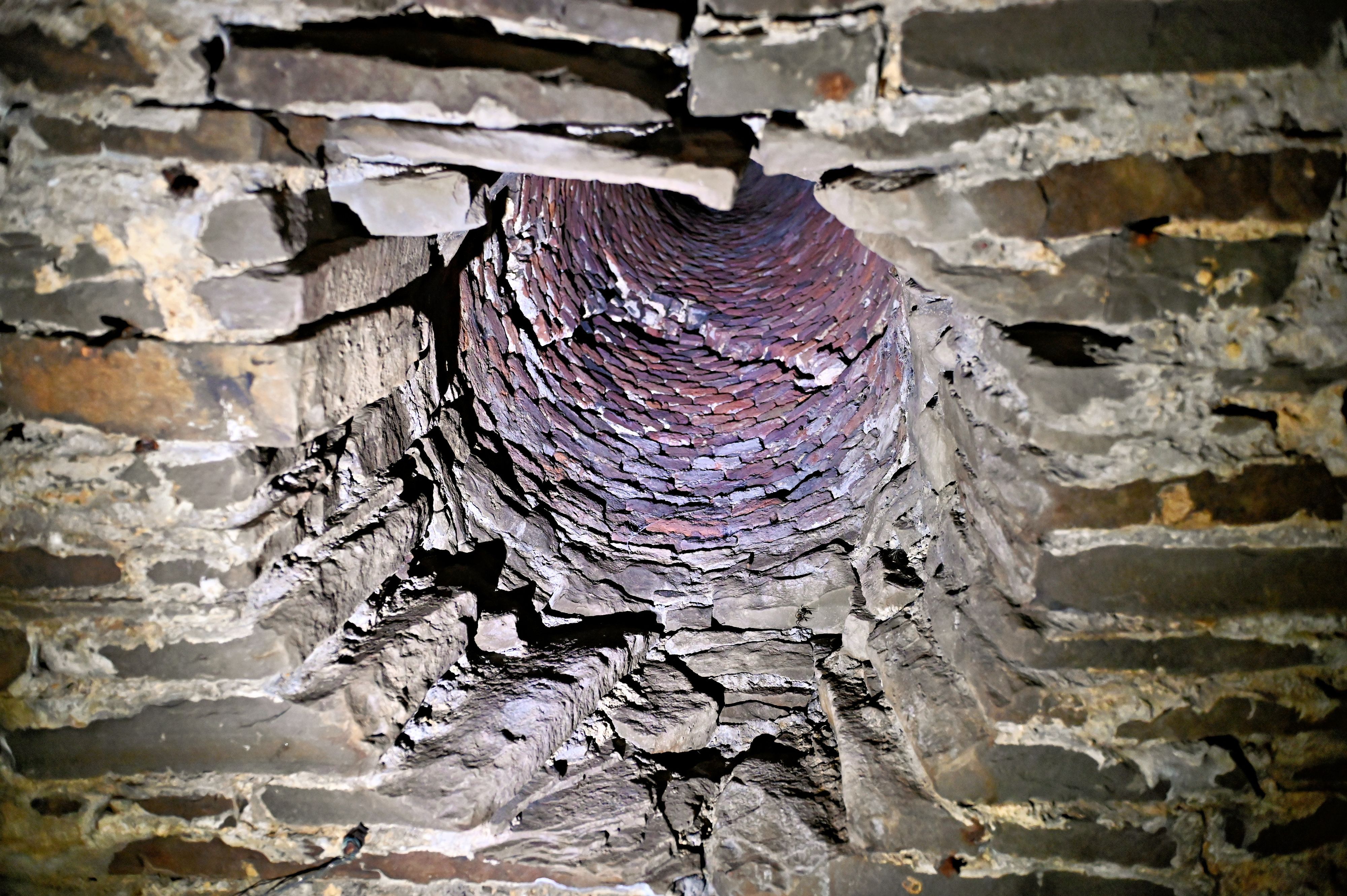 In einer Bruchsteinmauer ist ein Schacht zu sehen, der nach oben führt und durch den warme Luft abgeführt wurde.