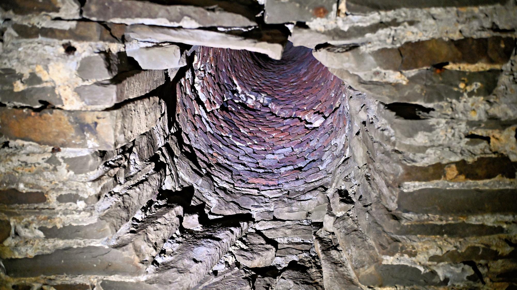 In einer Bruchsteinmauer ist ein Schacht zu sehen, der nach oben führt und durch den warme Luft abgeführt wurde.
