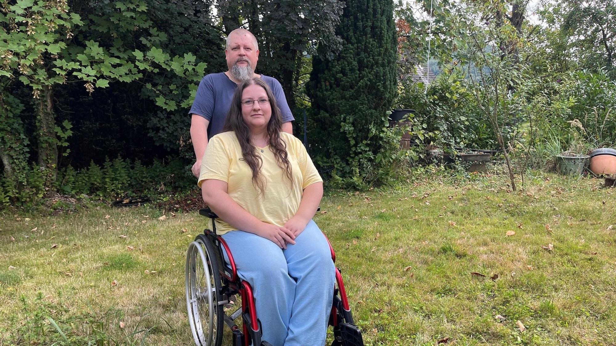 Der Vater steht hinter dem Rollstuhl, in dem Miriam sitzt.