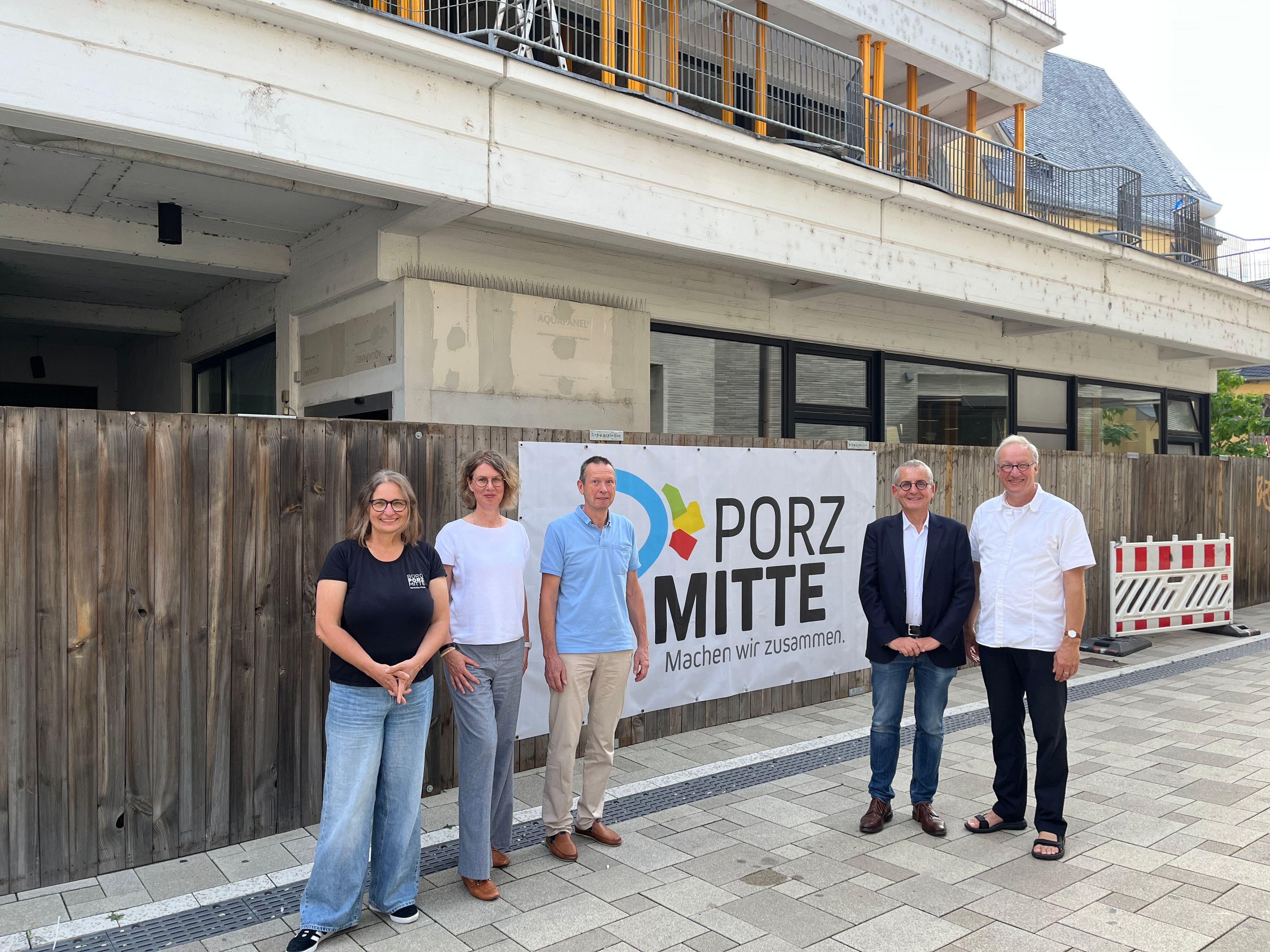 Fünf Personen stehen vor einem Bauzaun vor einem Rohbau.