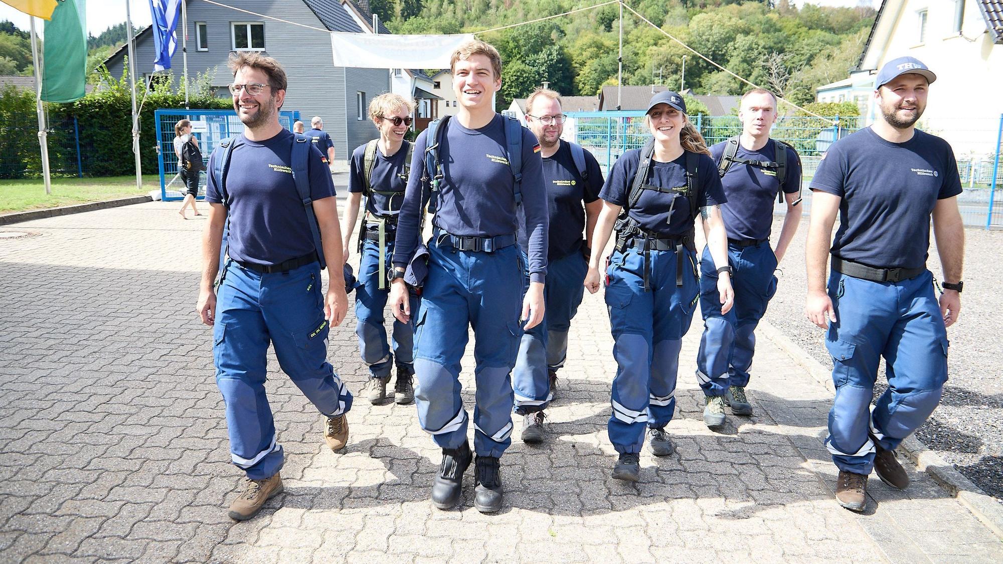 Mitglieder des THW Aachen gehen in Einsatzkleidung eine Straße entlang.