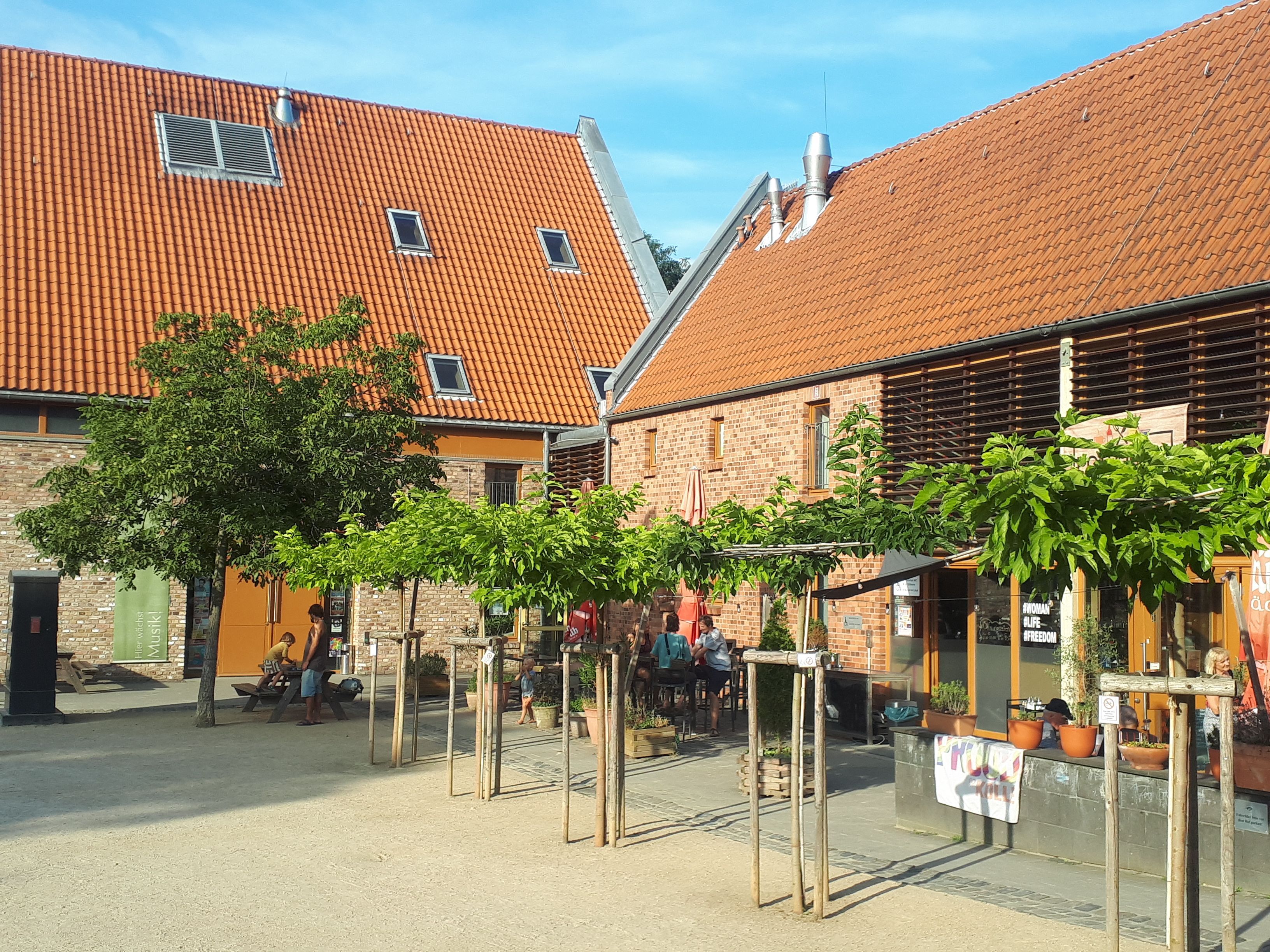 Zwei große Gebäude stehen hinter einer Baumreihe.
