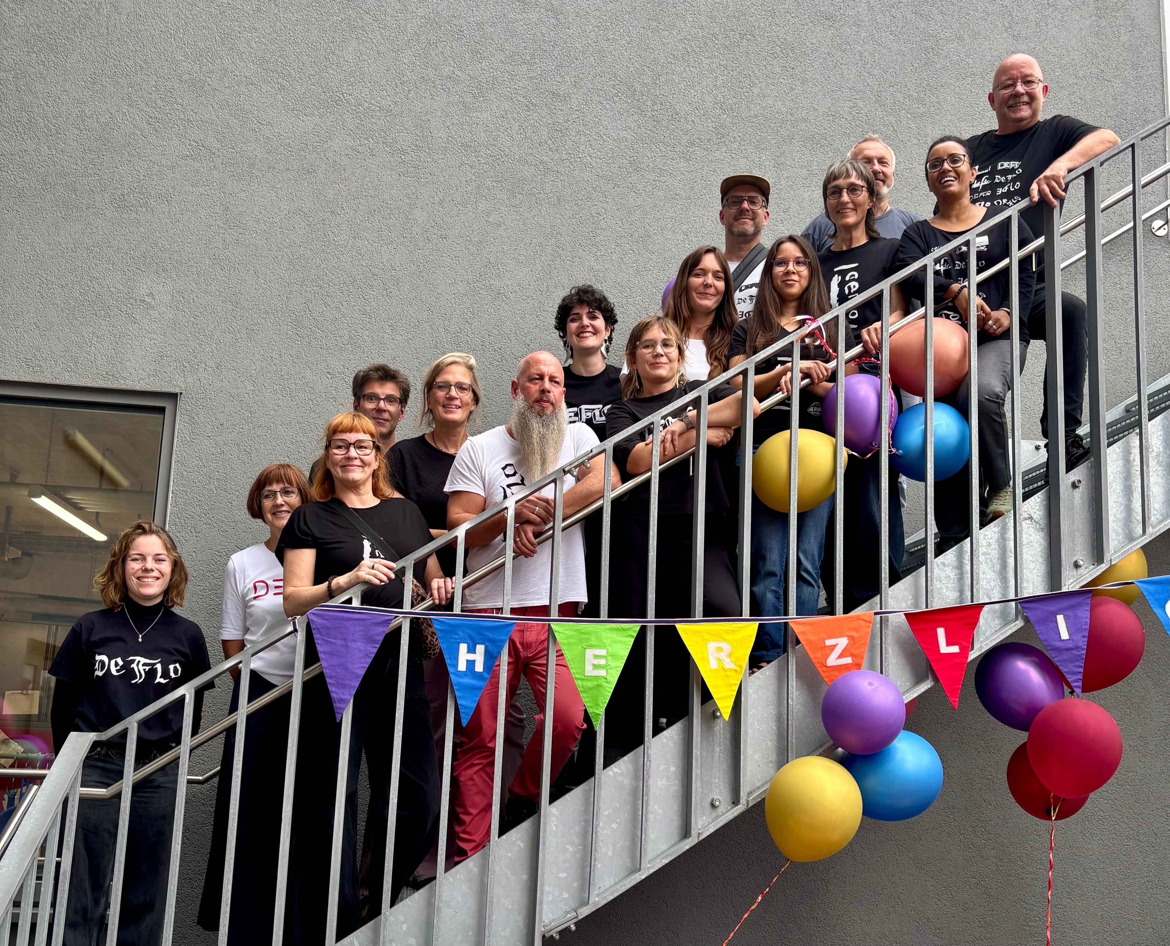 Viele Menschen stehen auf den Stufen einer Treppe. An der Treppe hängen Luftballons und eine Wimpelkette.