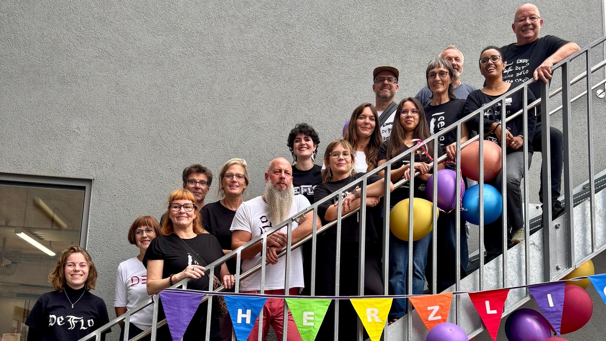Viele Menschen stehen auf den Stufen einer Treppe. An der Treppe hängen Luftballons und eine Wimpelkette.